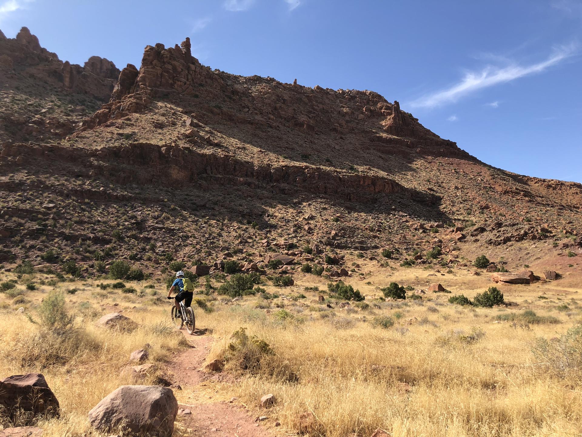 Person mountain biking on a desert trail with large rock formations.