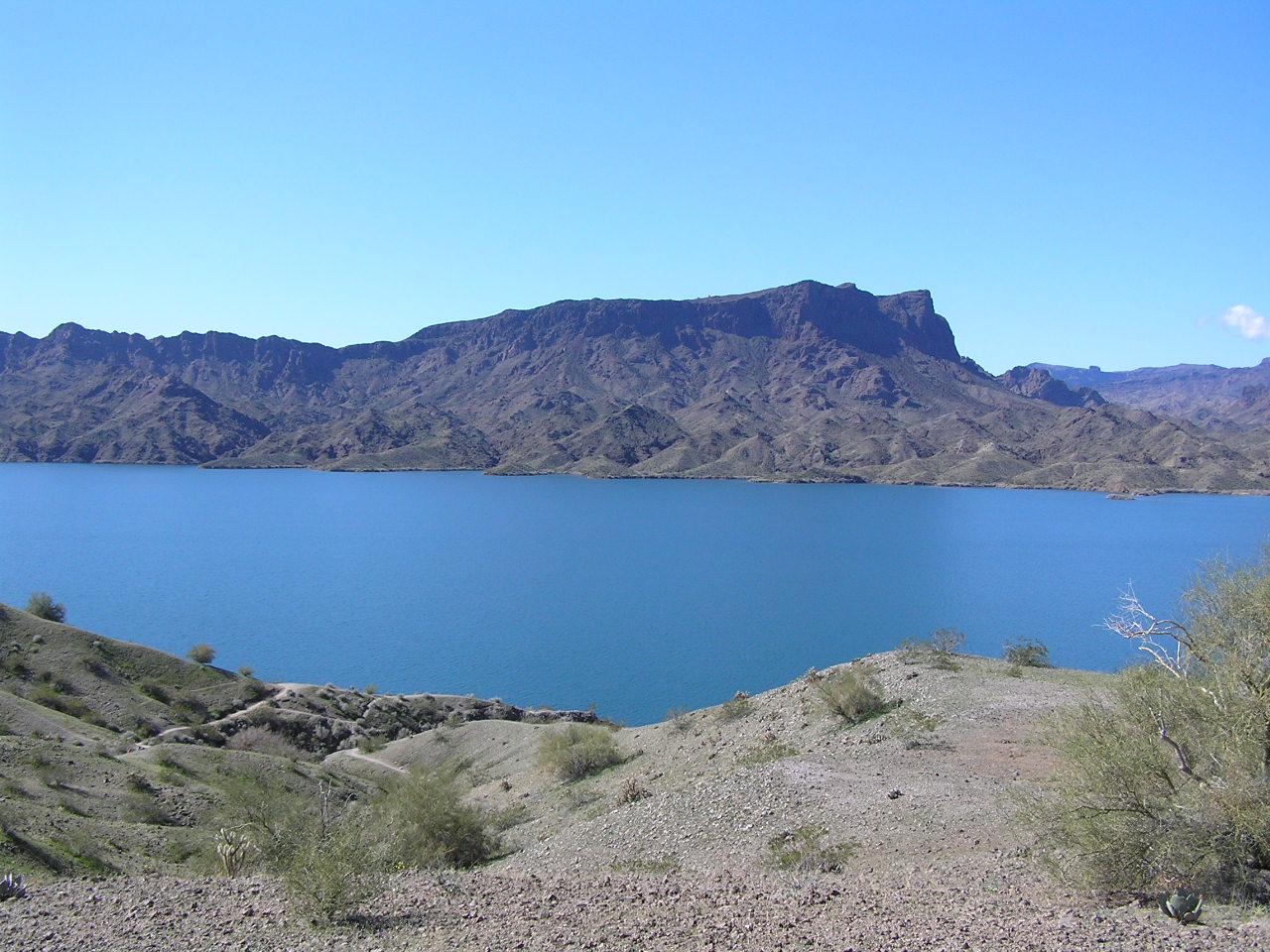 A wide blue lake surrounded by arid mountains under a clear sky.