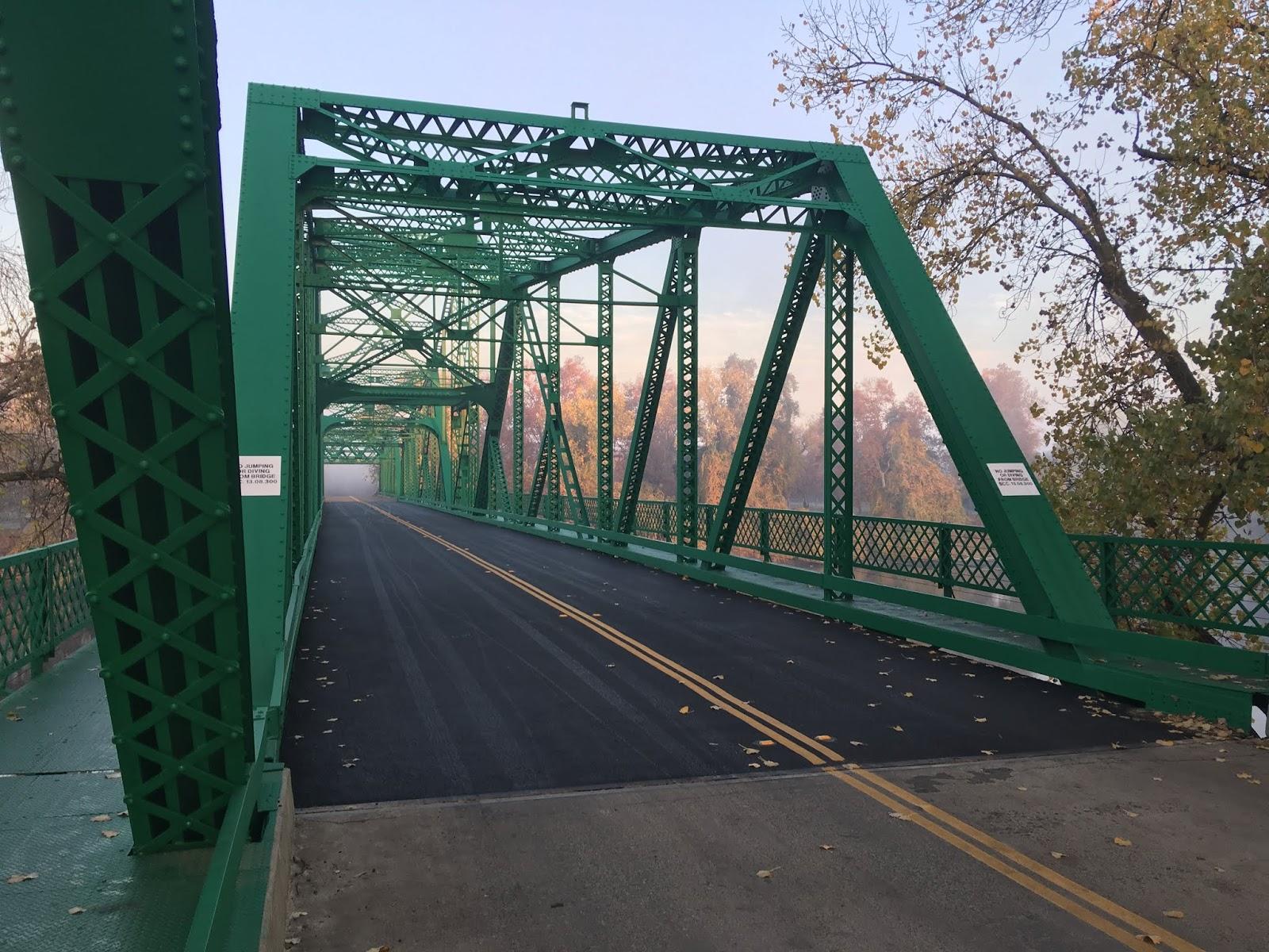A green metal truss bridge with a paved road, surrounded by trees.