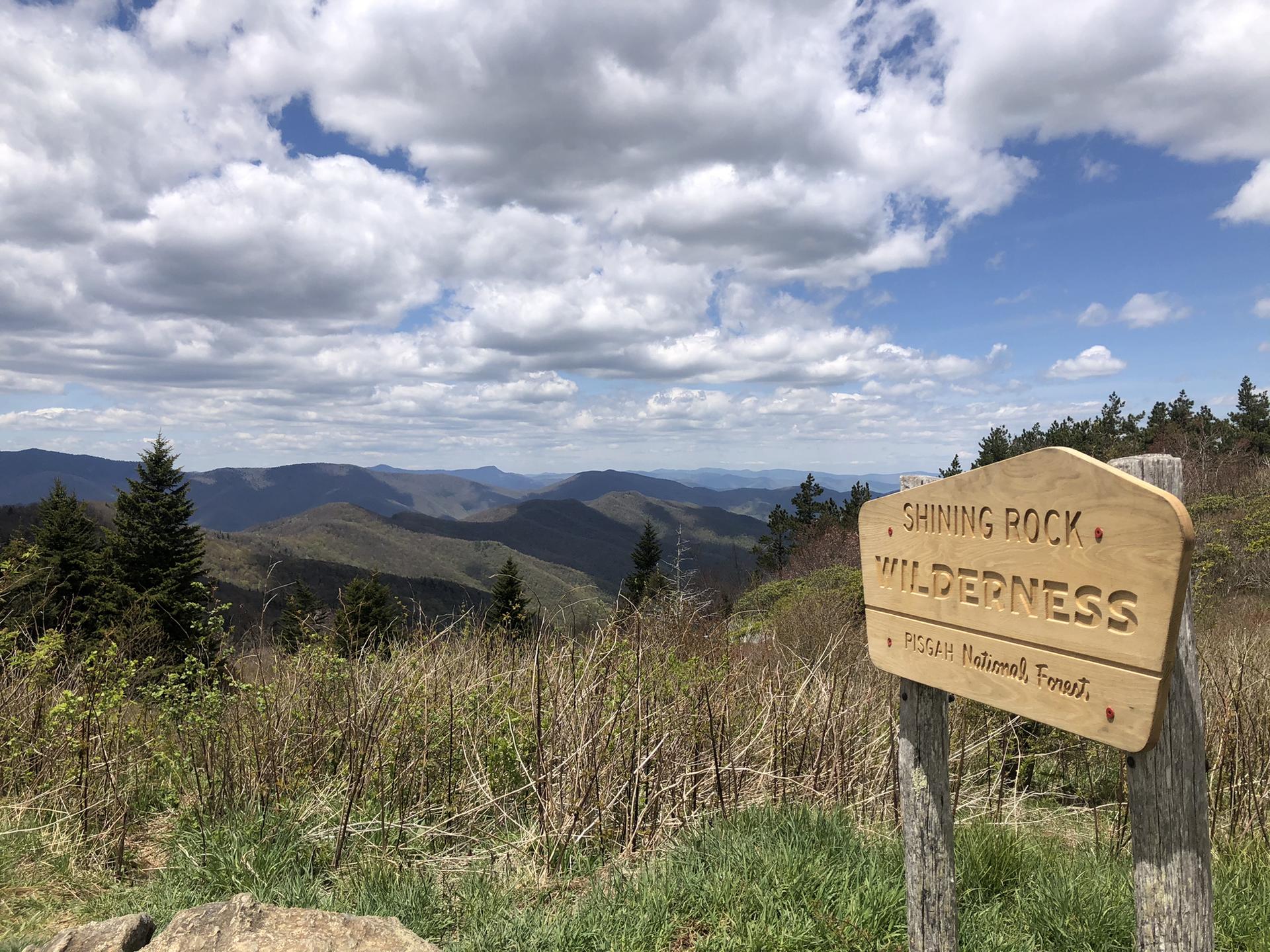 Wooden sign in foreground with a vast mountain range under a cloudy sky.