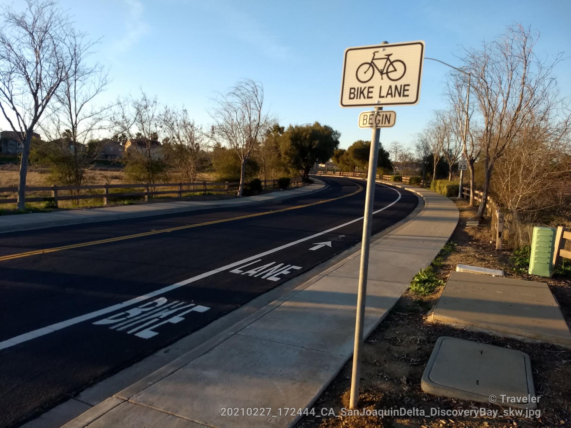 A bike lane sign stands beside an empty paved path on a clear day.