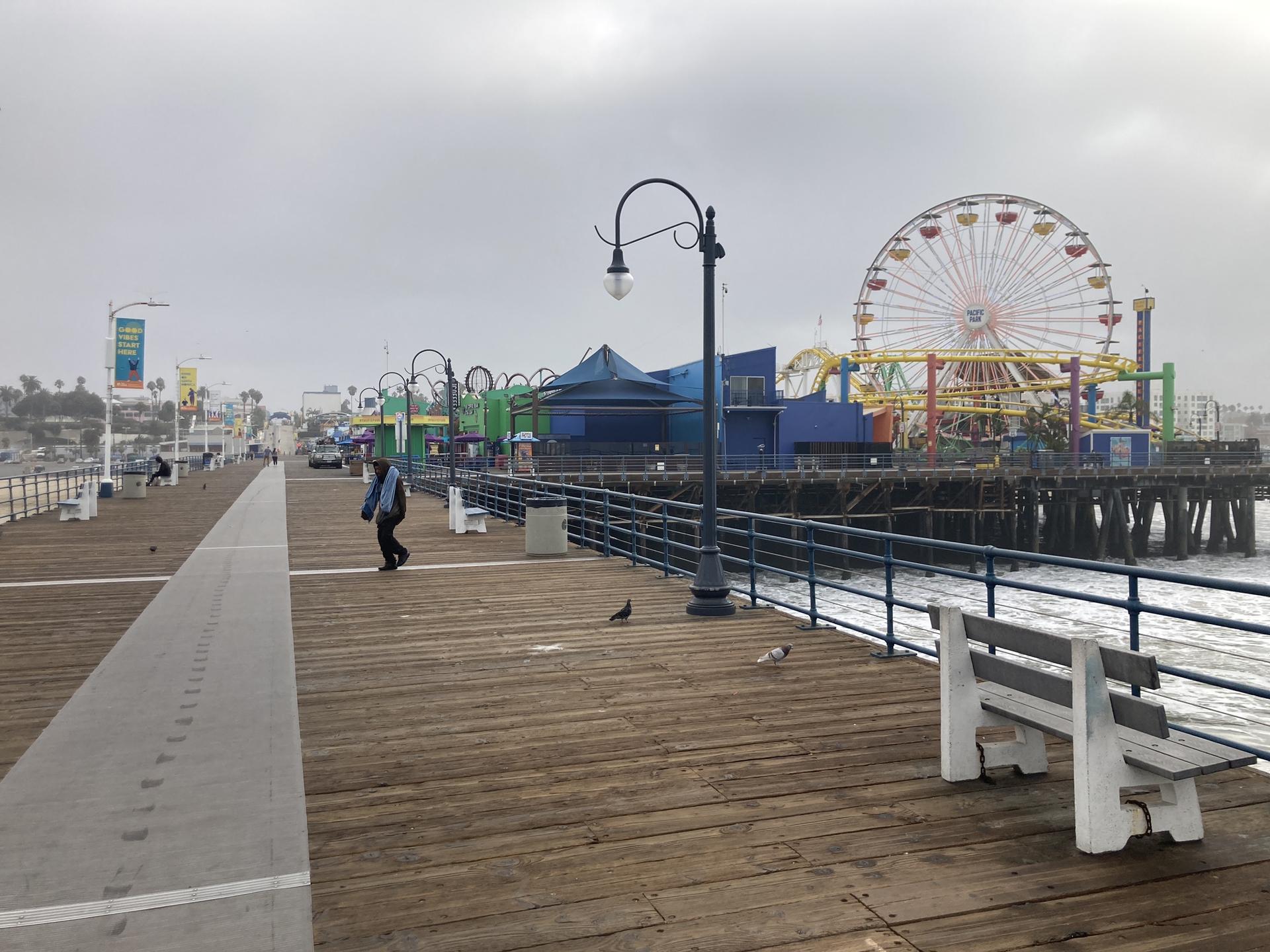 A wooden pier with a Ferris wheel and amusement rides under an overcast sky.