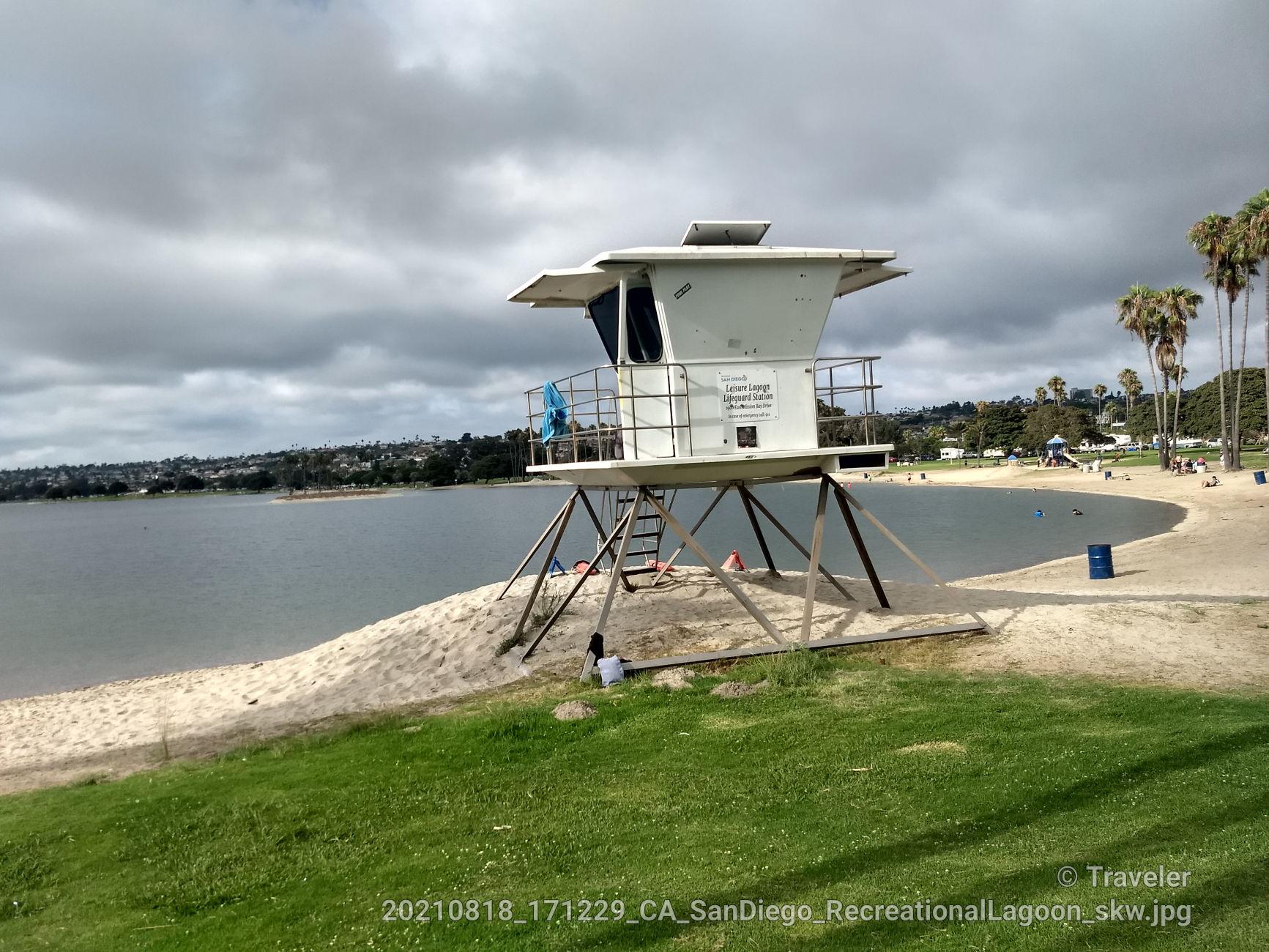 White lifeguard tower on a sandy beach by calm water under cloudy skies. One person.