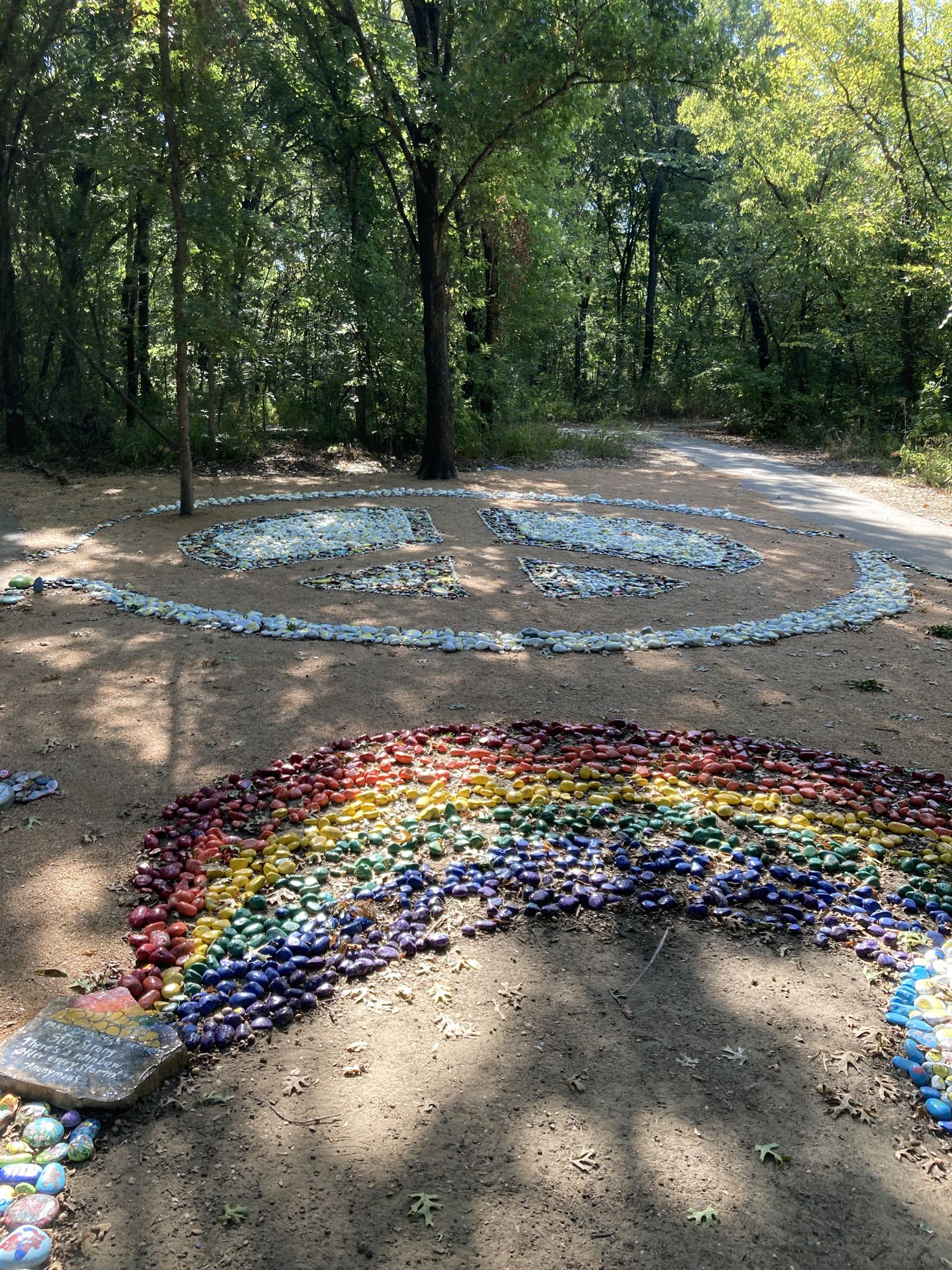 Colorful stone rainbow and peace sign art on dirt ground, surrounded by trees. - Bear Creek Trail