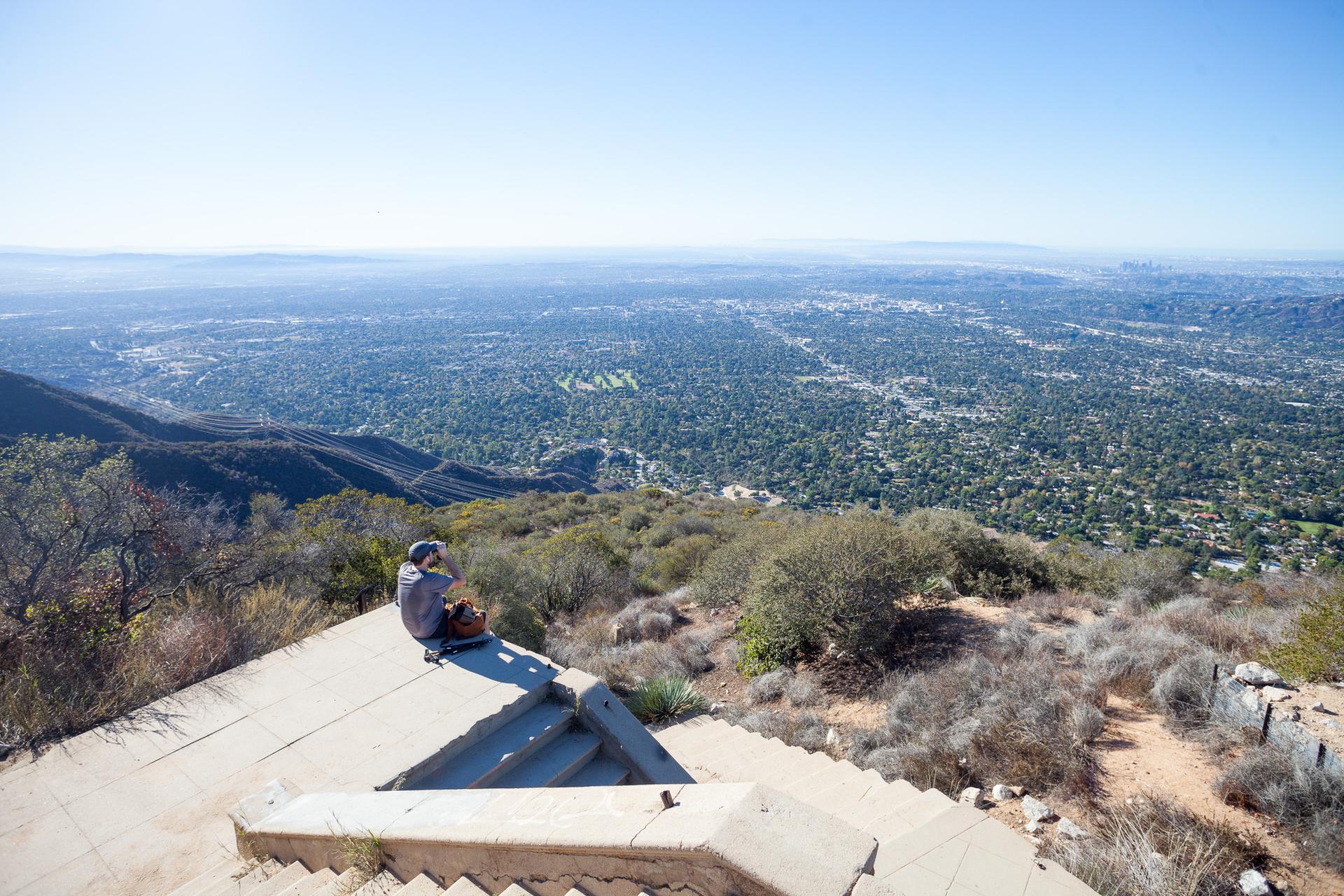 Person sitting on concrete steps overlooking a vast green valley.