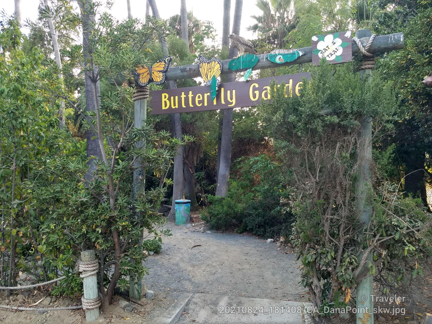 A wooden sign for 'Butterfly Garden' over a shaded path with lush greenery.