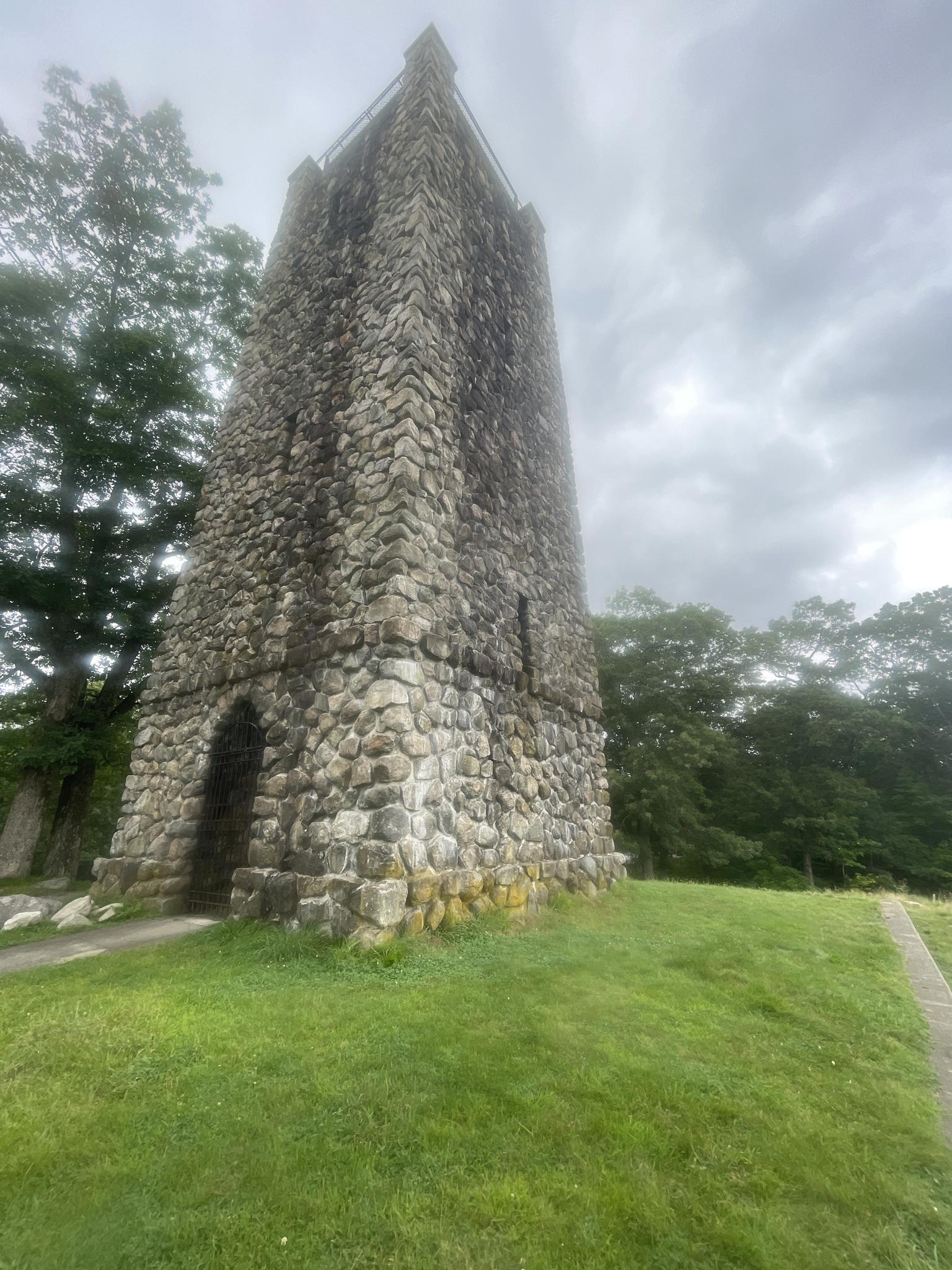 Tall stone tower on a grassy hill under an overcast sky.