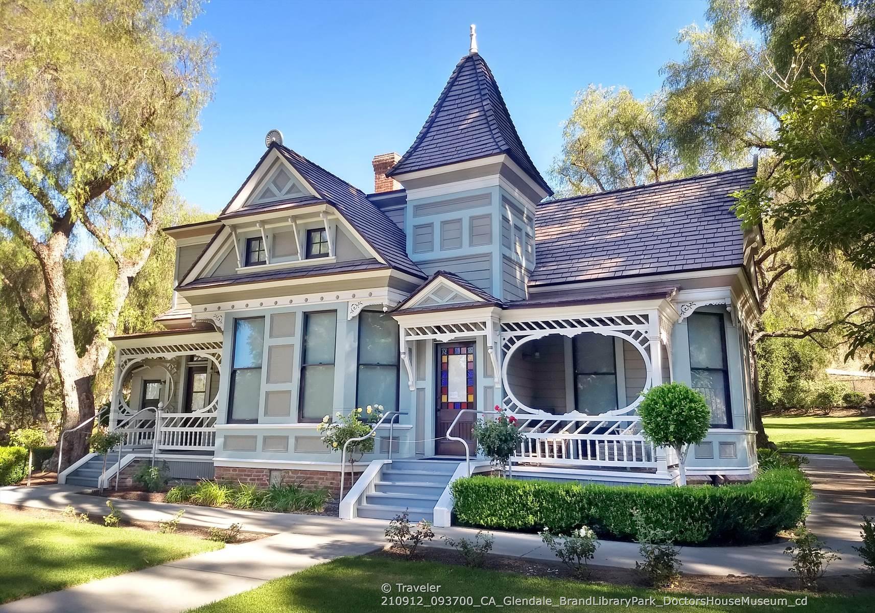 An ornate Victorian house with a turret, surrounded by green trees and lawn.
