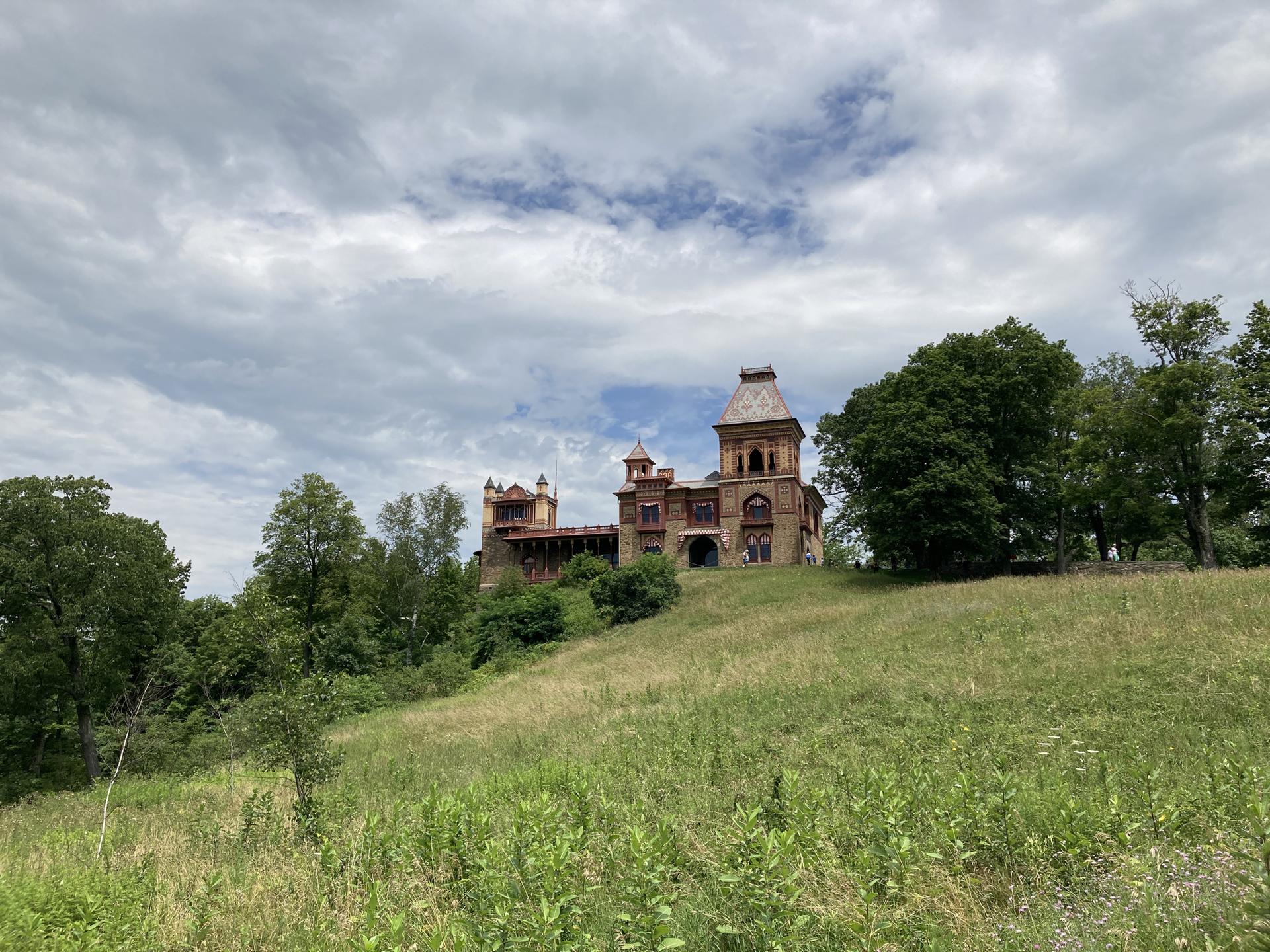 Ornate historic building on a grassy hill under a cloudy sky.