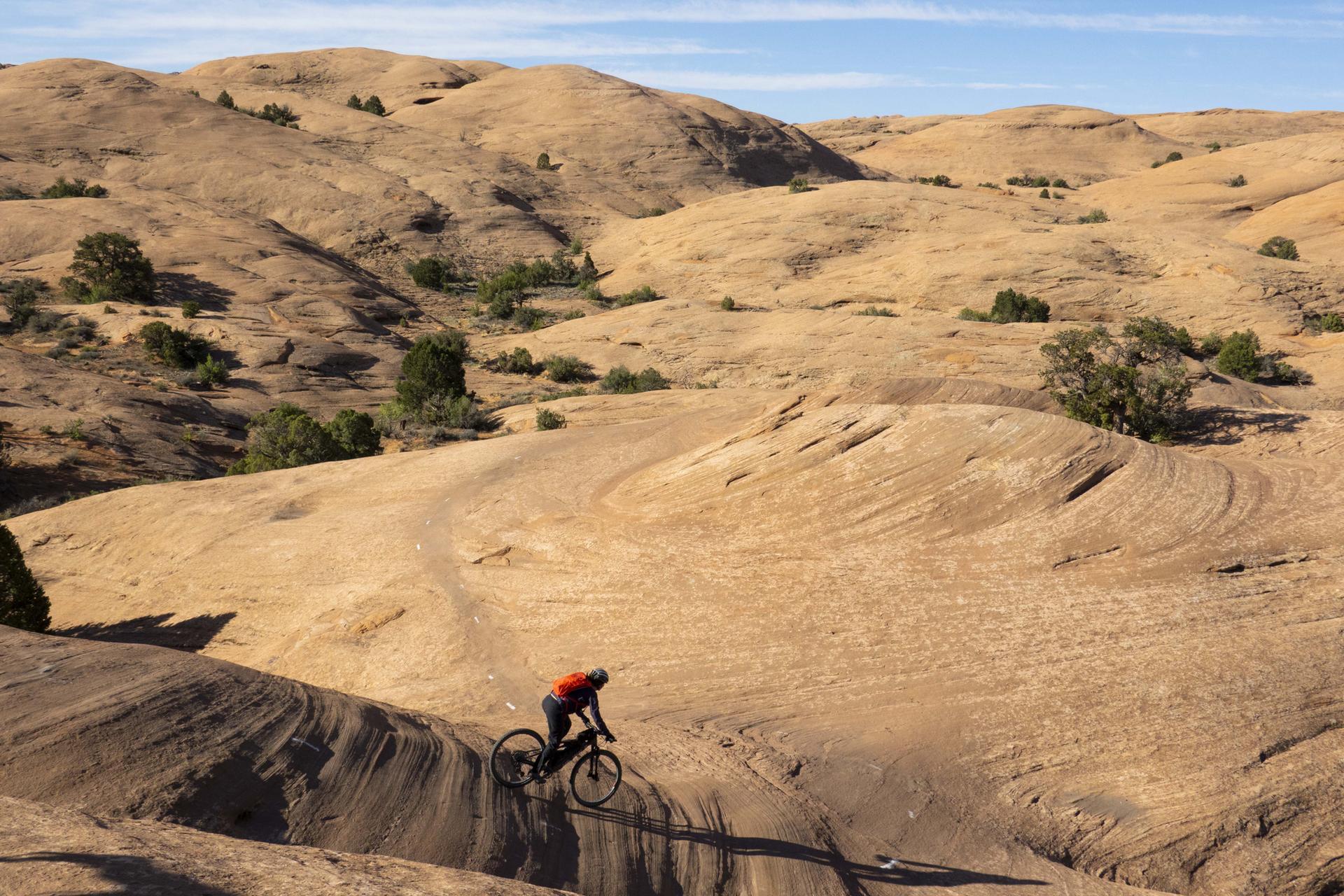 Mountain biker descending a sculpted rock formation in a desert landscape.