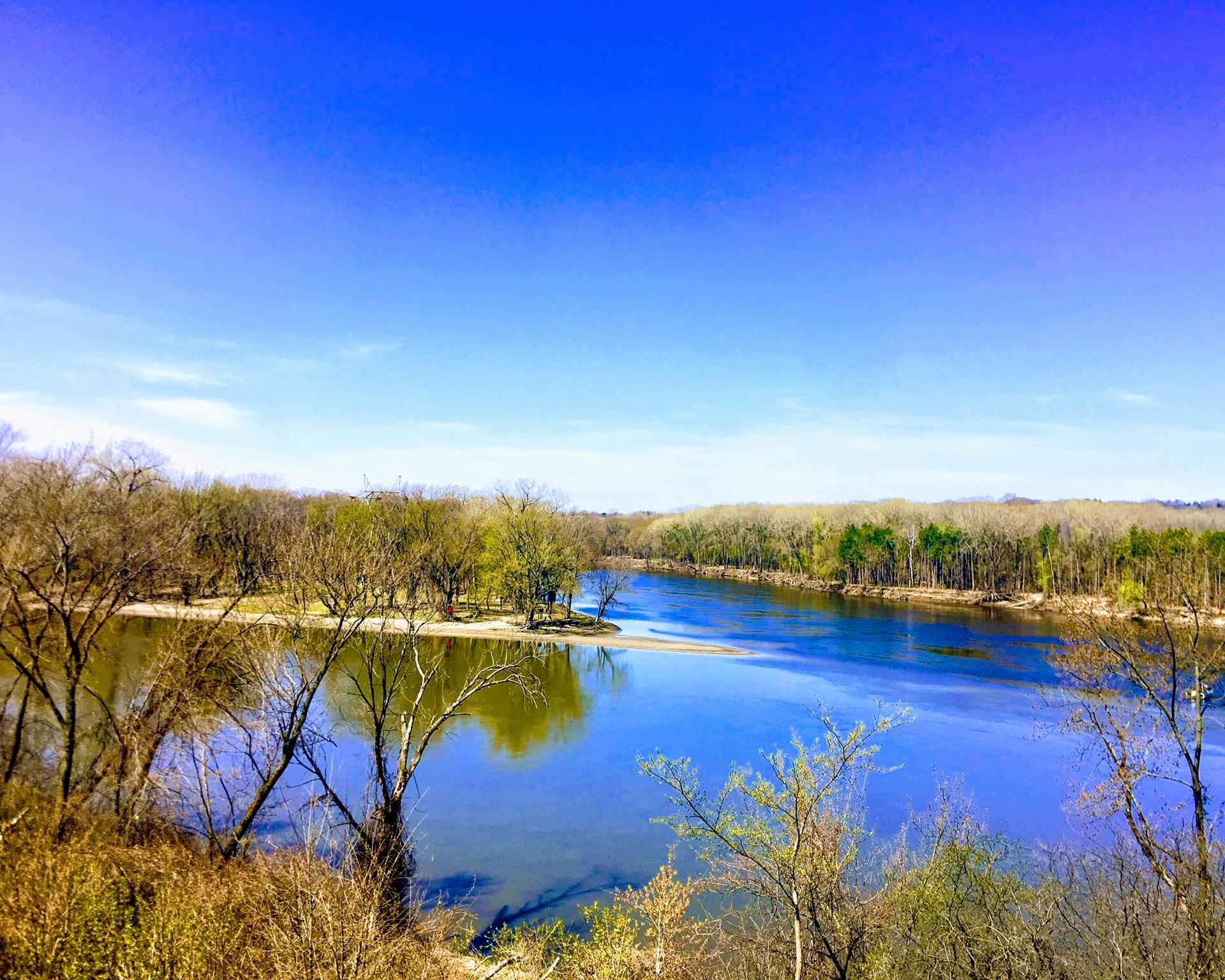 Brightly lit river flowing through a forested landscape under a vibrant blue sky.