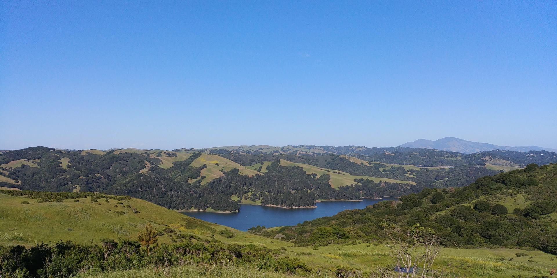 Panoramic view of a blue lake surrounded by green, forested hills.