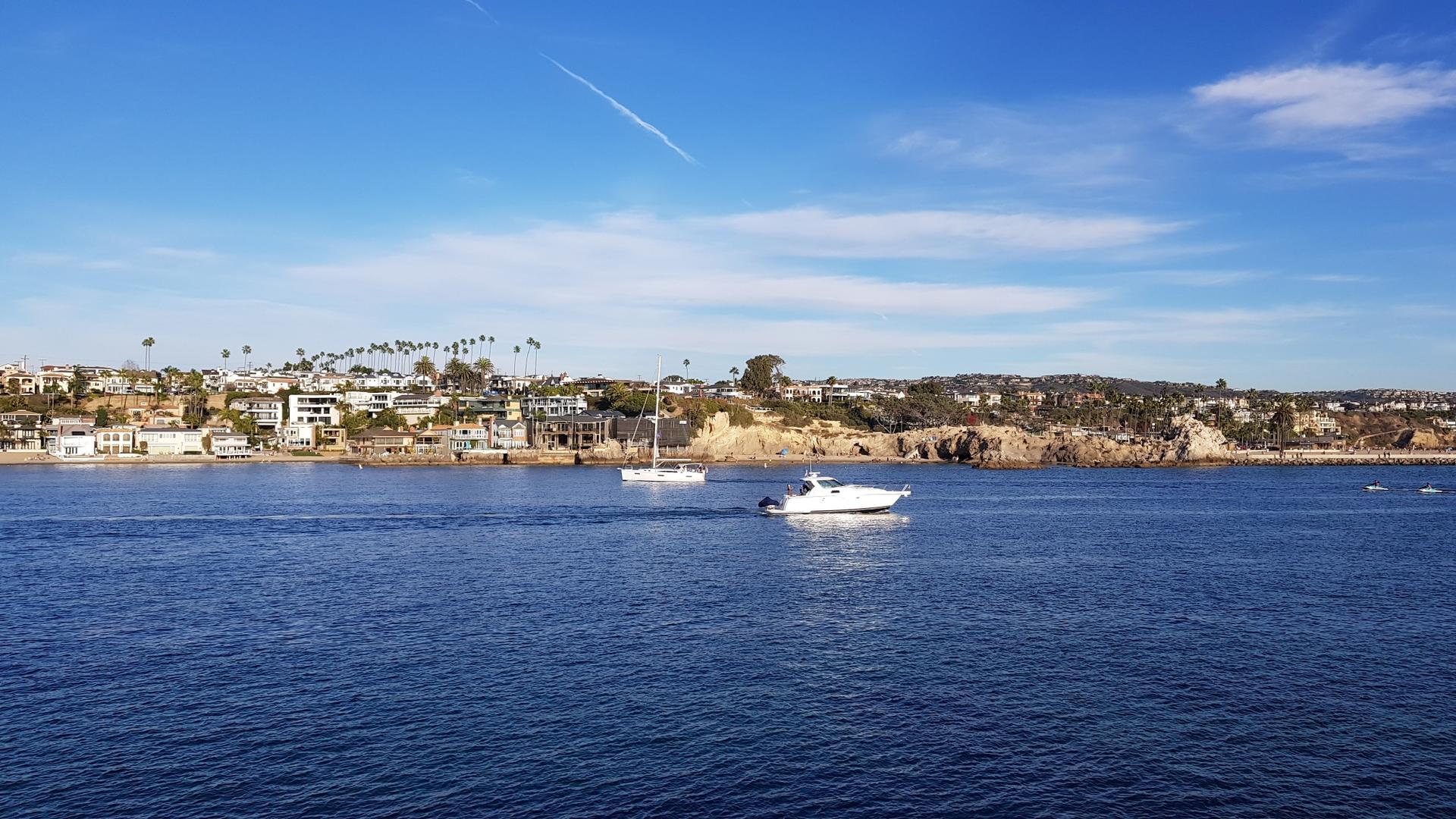 Two boats on calm blue water with a sunny coastal town in background.