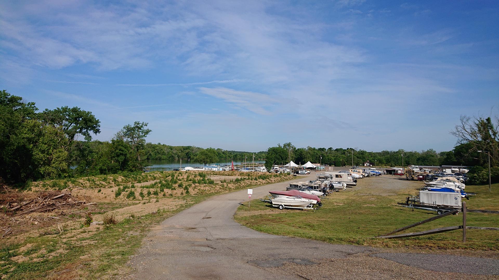 A sunny boat storage lot next to a body of water and green trees.