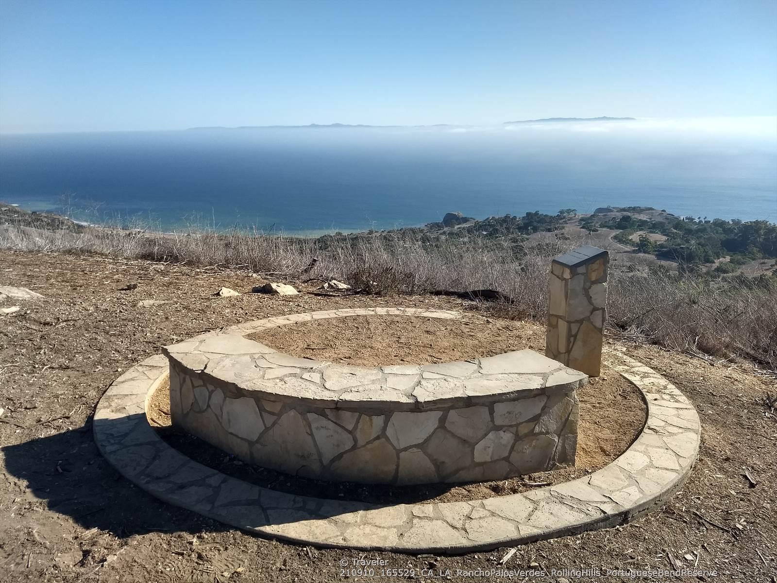 Stone bench and monument overlooking a vast ocean and distant land.