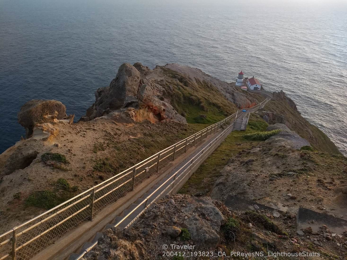 Fenced walkway leading to a lighthouse on a rocky cliff at sunset. - Point Reyes Lighthouse Trail