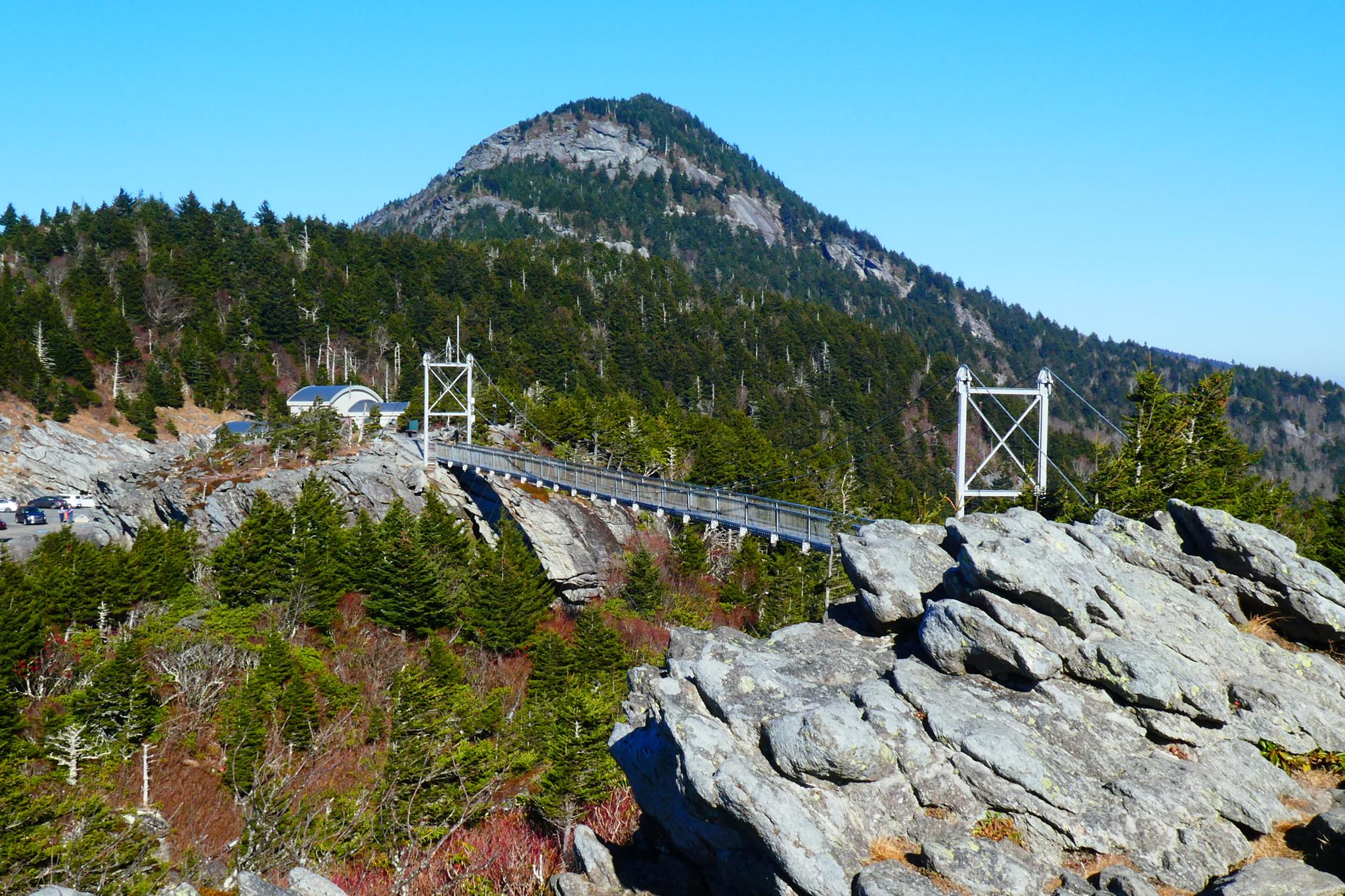 Mountain peak, suspension bridge, and rocky foreground under clear blue sky.