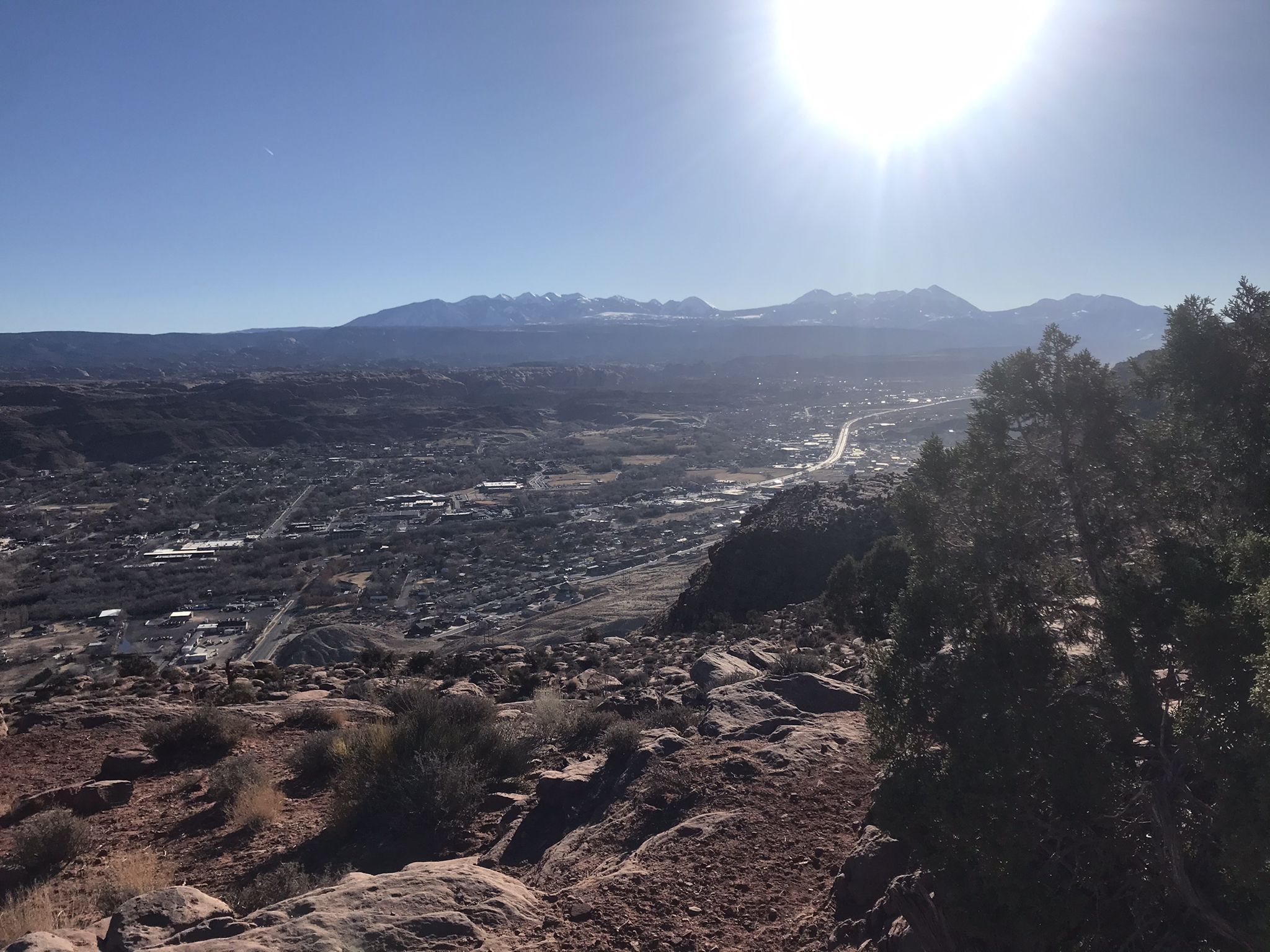 A bright sun shines over a town nestled among mountains and desert. - The Stairmaster – Moab Rim overlook loop from Scott Matheson Wetlands Preserve