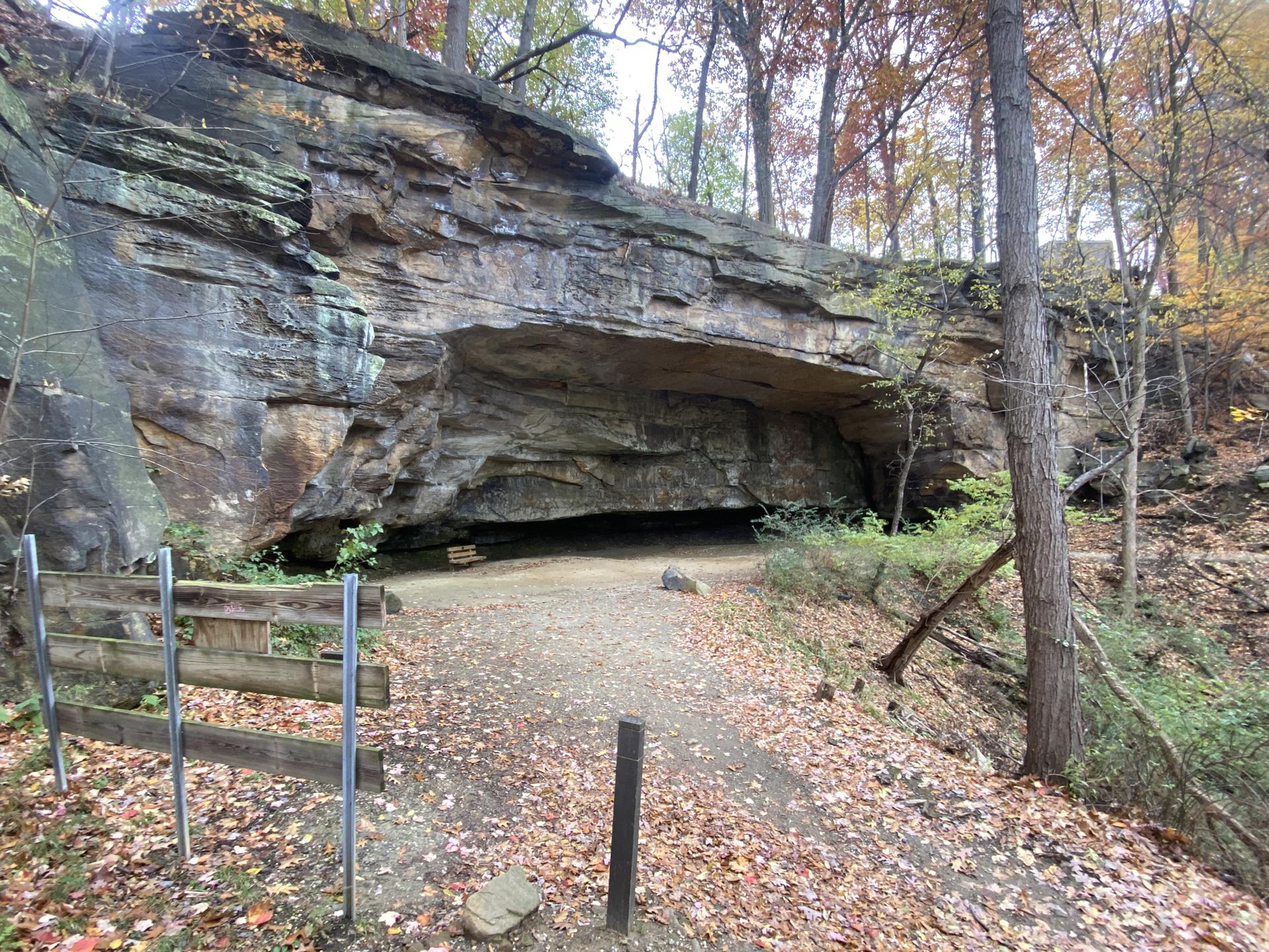 Large rock overhang forming a cave entrance, with a dirt path.