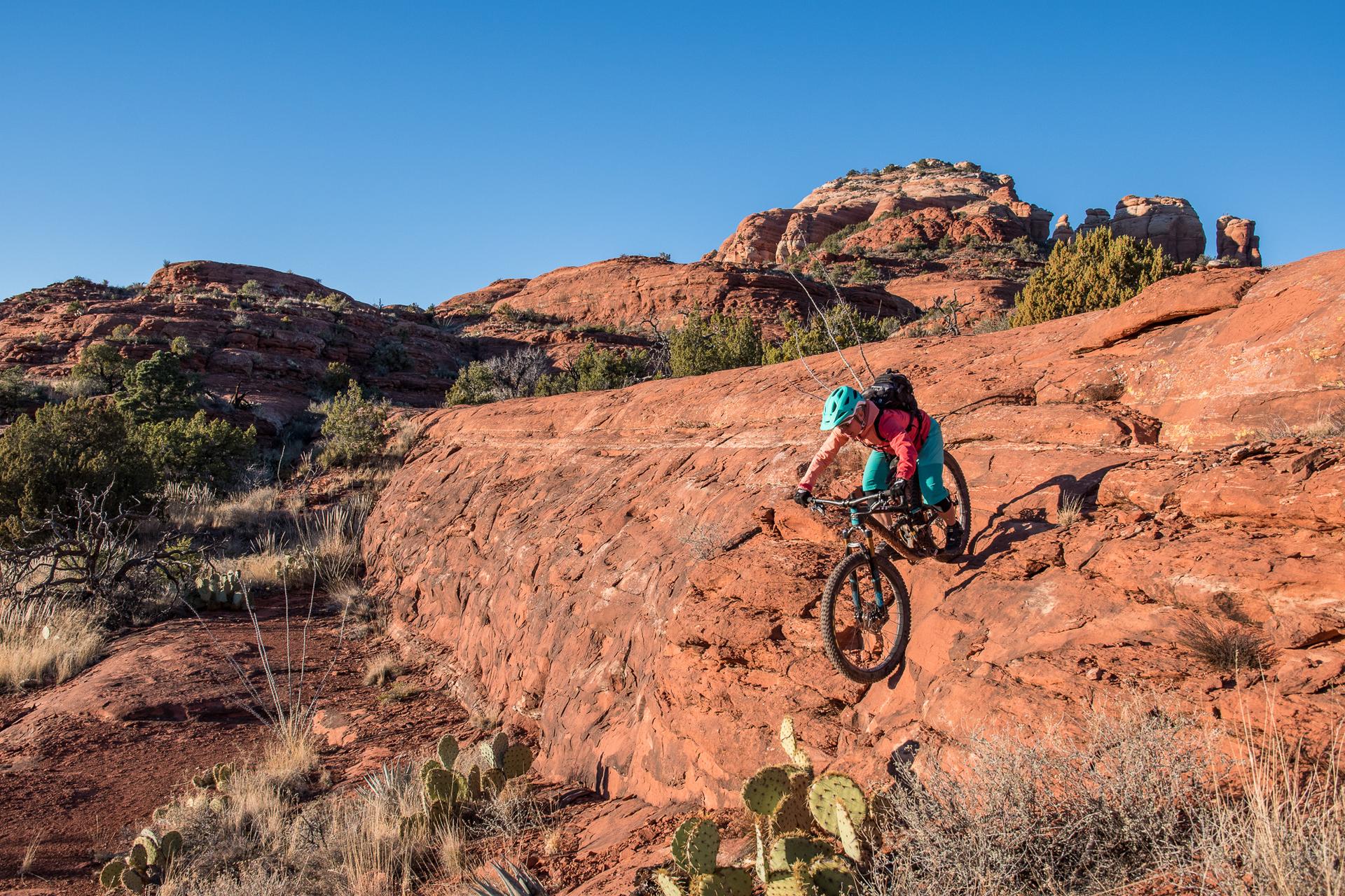 Mountain biker descending a red rock slope under a clear blue sky.