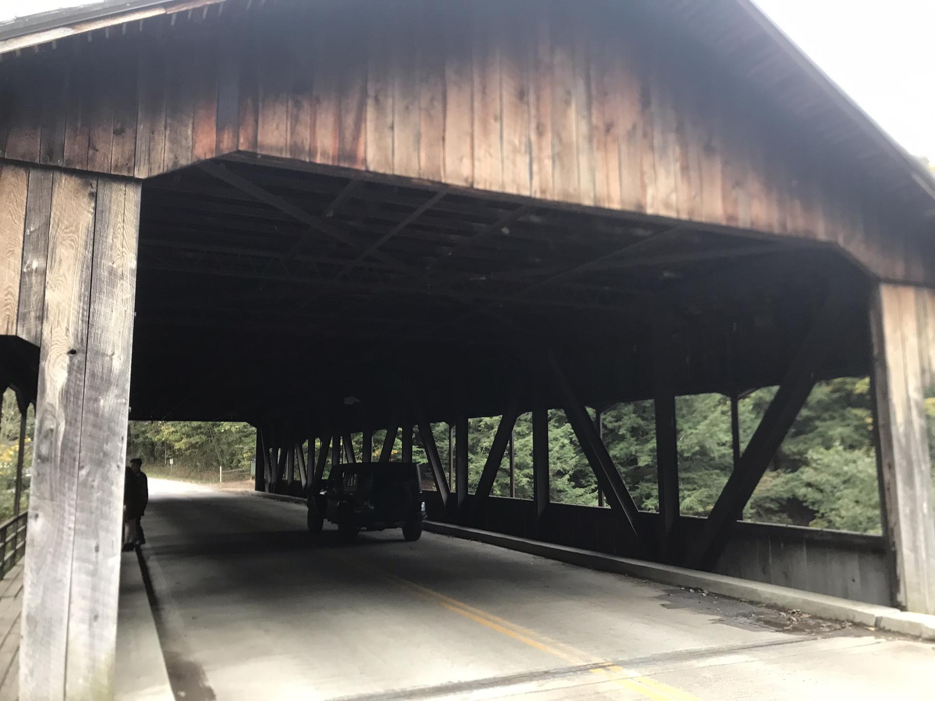 A dark wooden covered bridge with a vehicle and person inside.