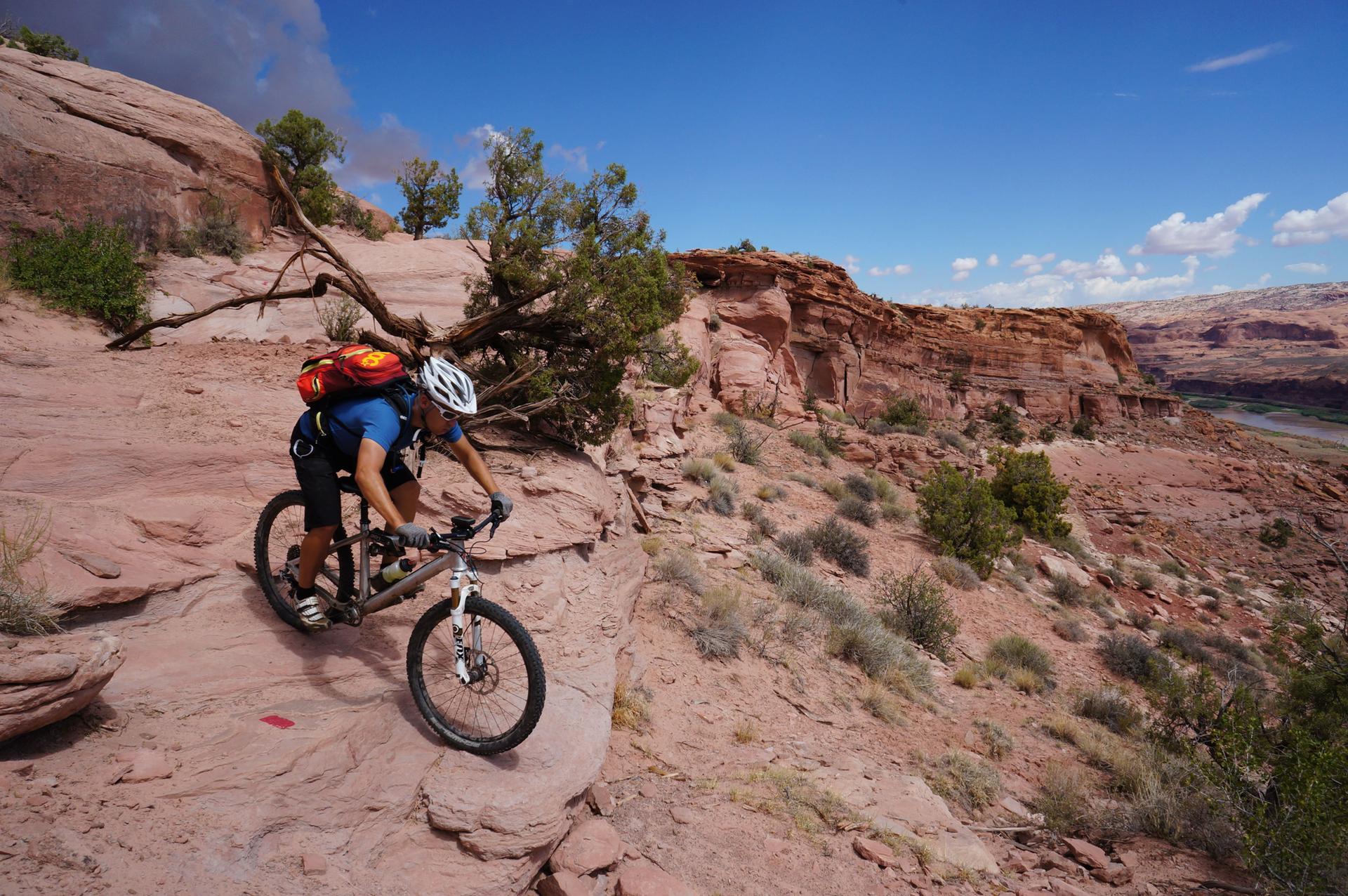 Mountain biker on a rocky trail overlooking a canyon under bright sun.