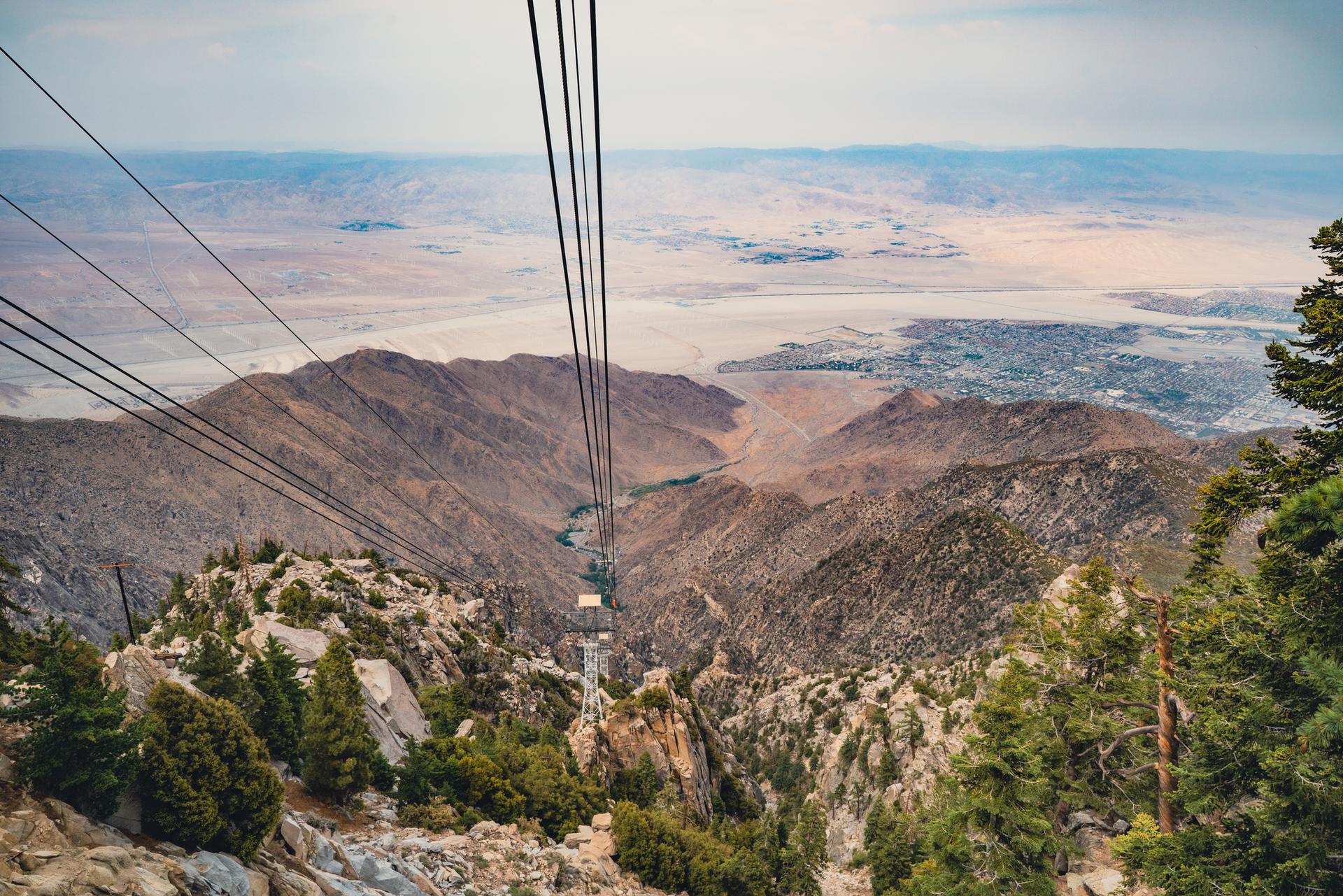 A dramatic aerial view from a cable car over rugged mountains and a valley.