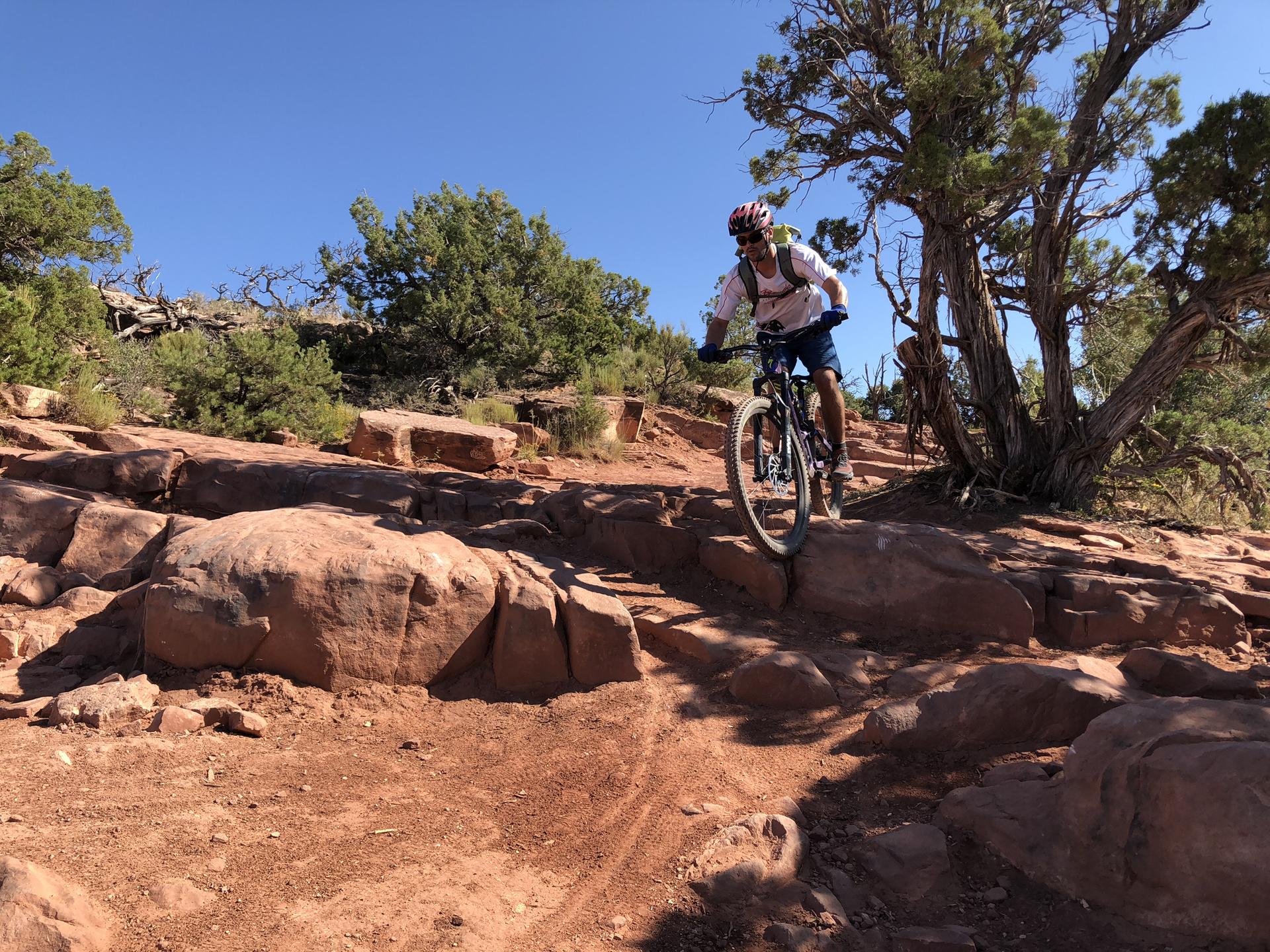 Mountain biker navigating rocky terrain under a bright blue sky.