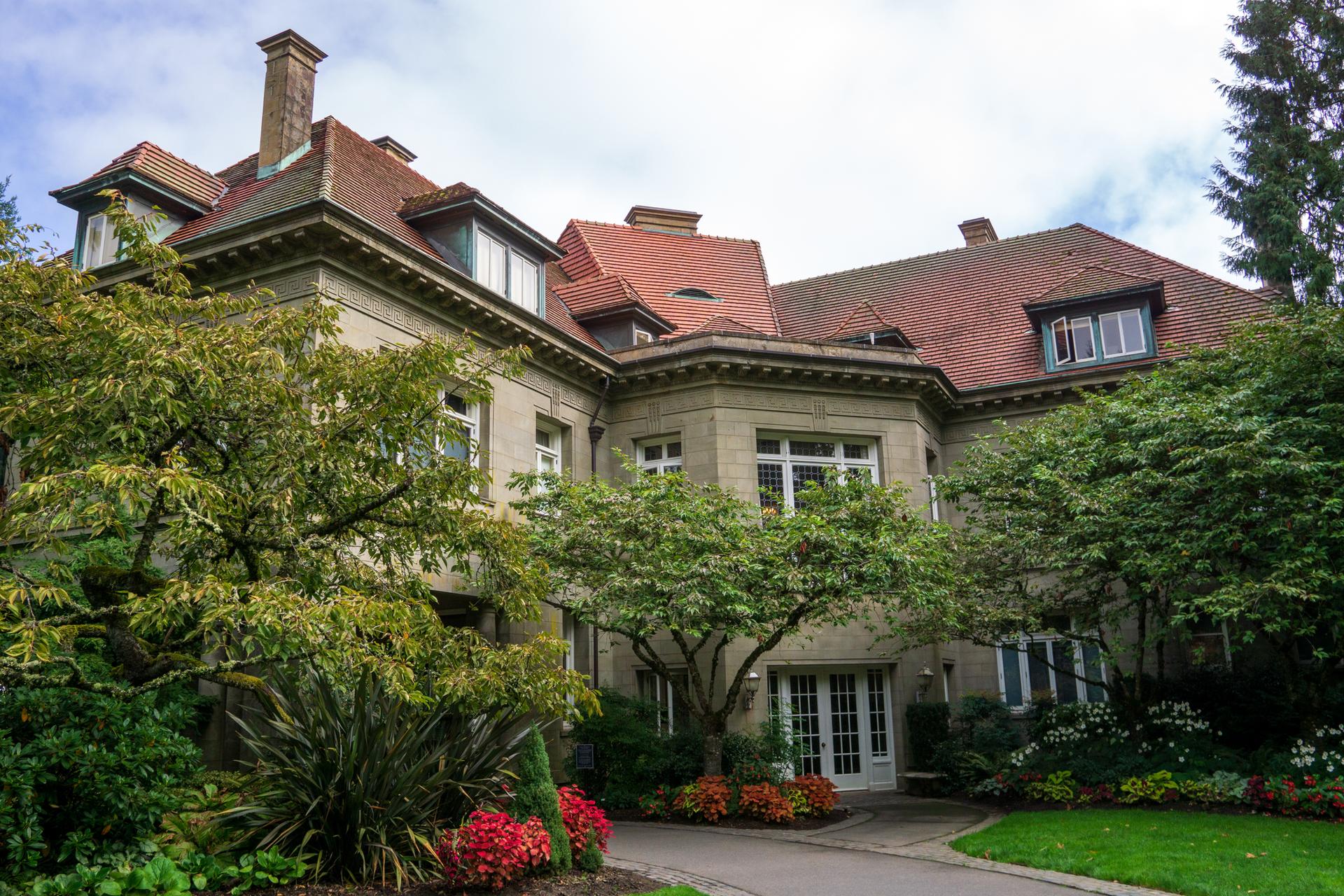 Ornate stone mansion with red tile roof, surrounded by lush green landscaping.