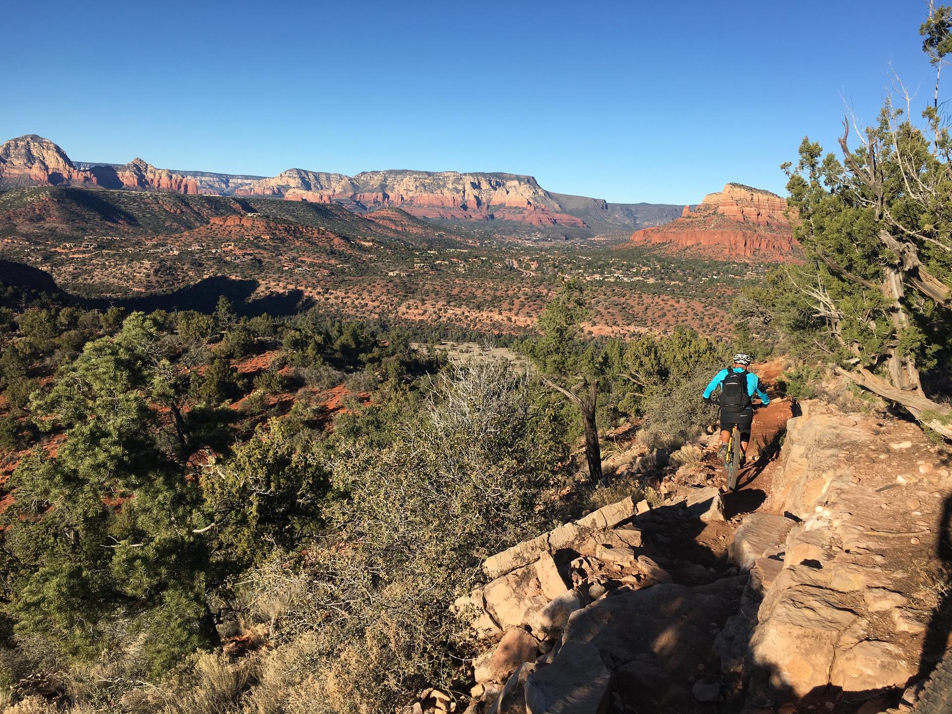 Mountain biker on a rocky trail overlooking a vast red rock landscape.