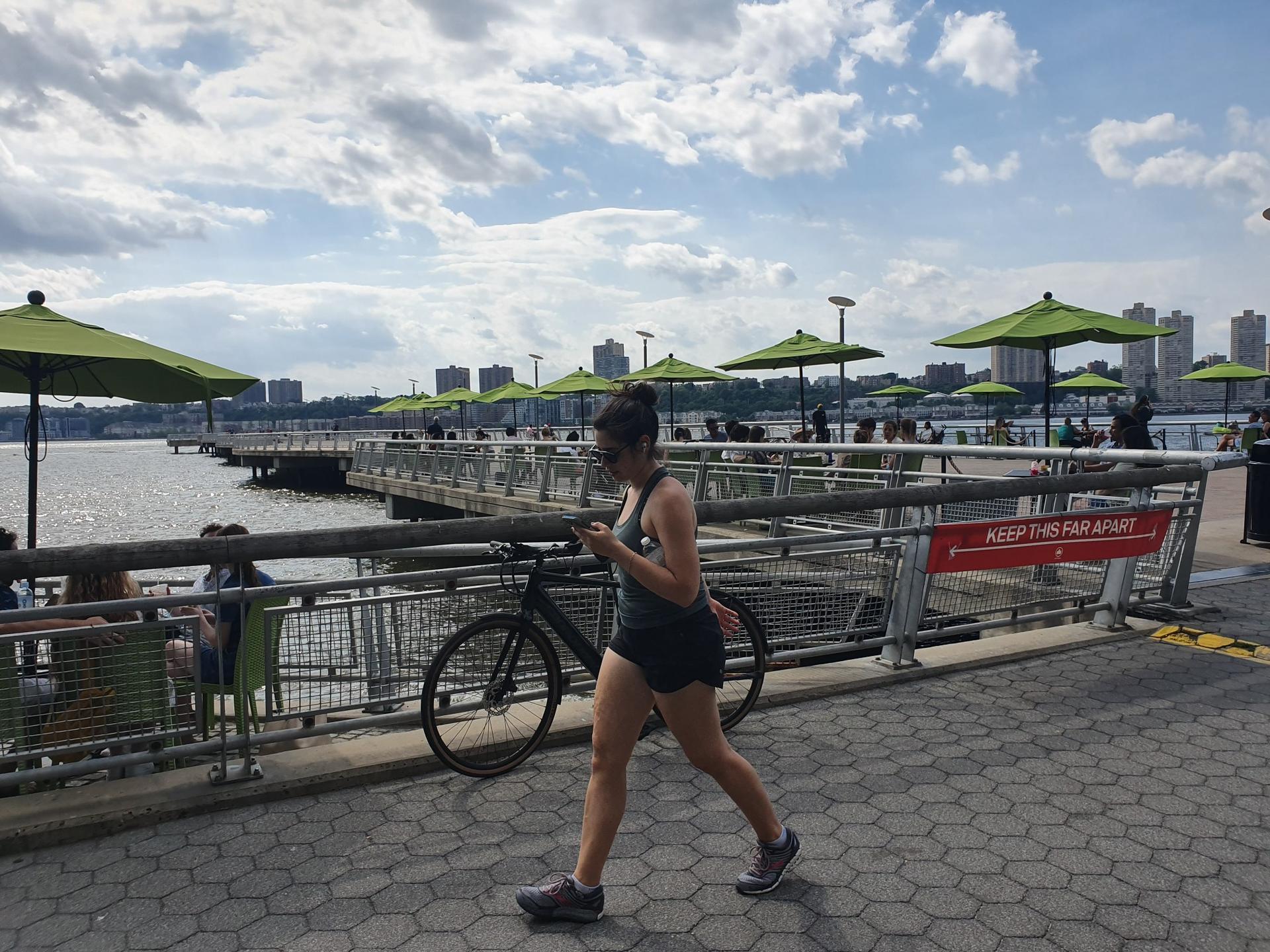Woman walking on a paved pier by water with green umbrellas and city.