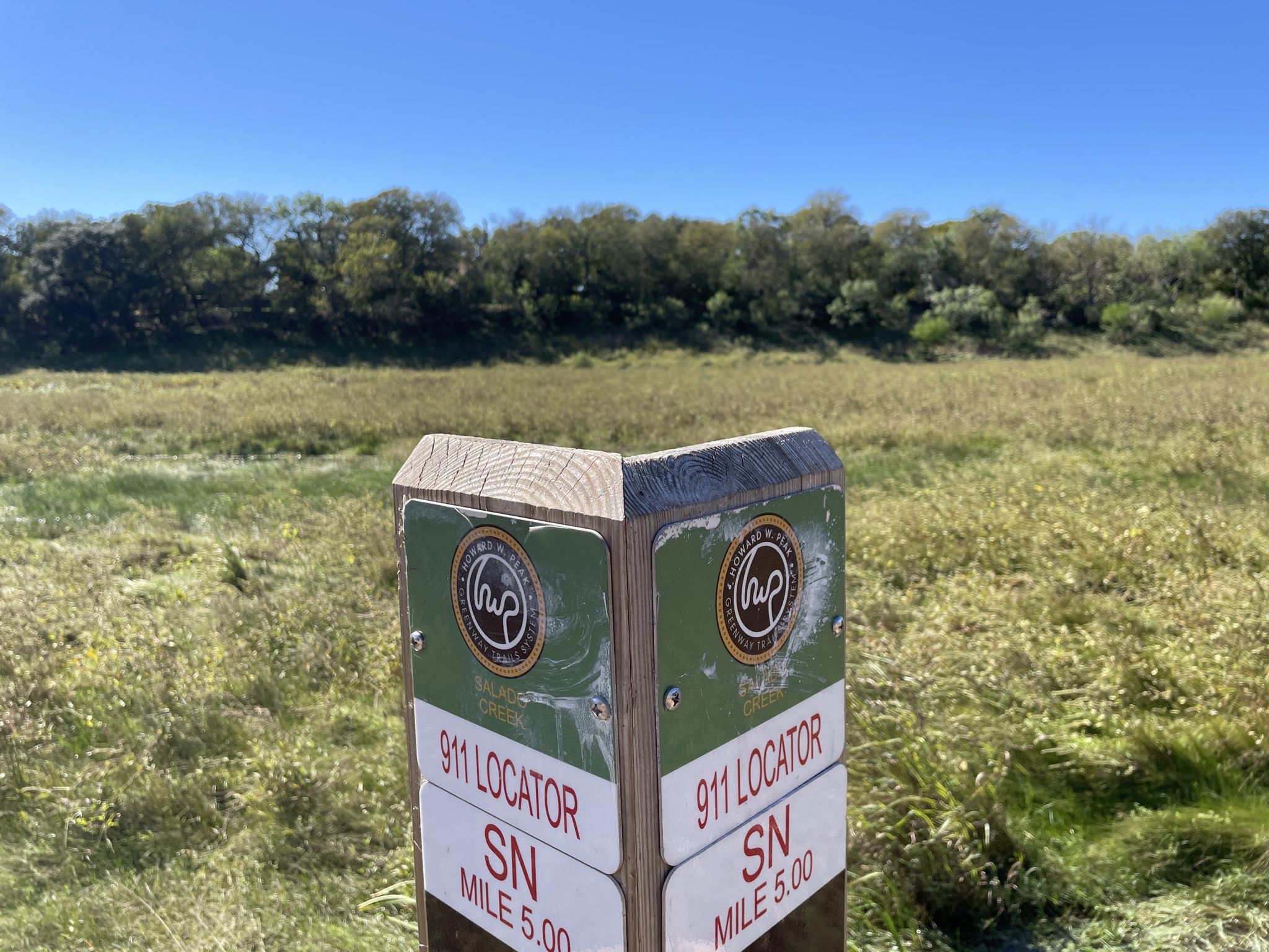 A trail marker stands in a vast grassy field under a clear blue sky. - Robert L.B. Tobin Park – Morningstar Boardwalk loop from McNay Art Museum