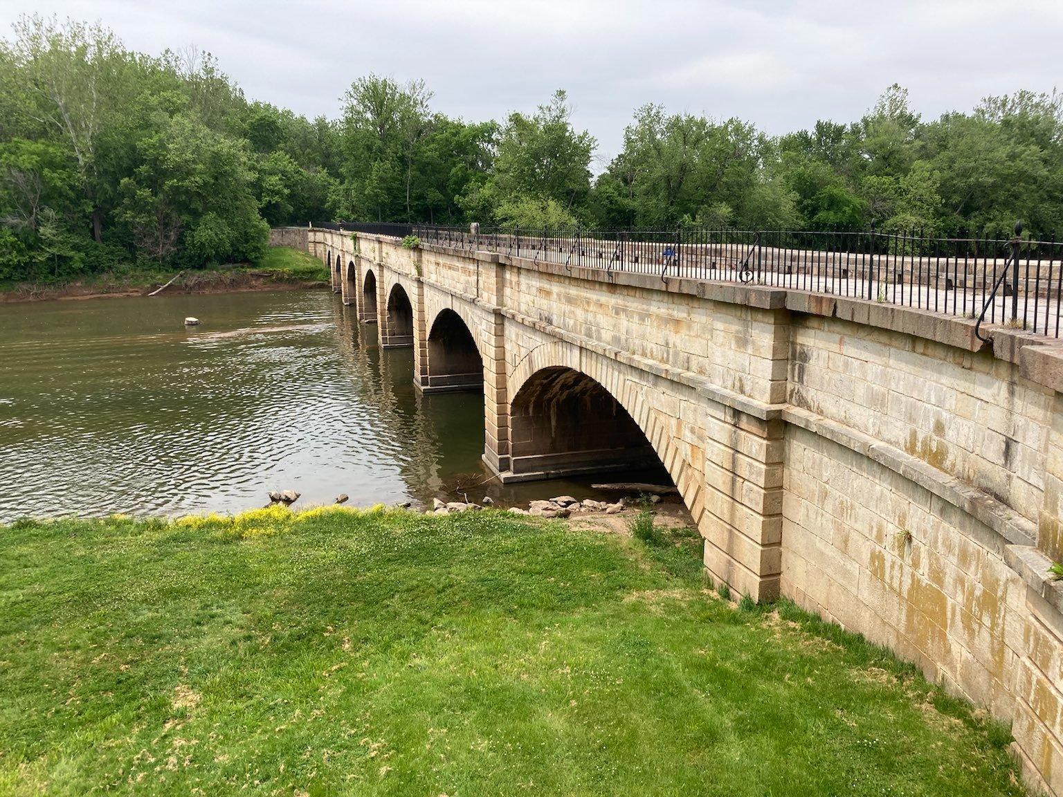 A long stone arch bridge spans a calm river under an overcast sky.