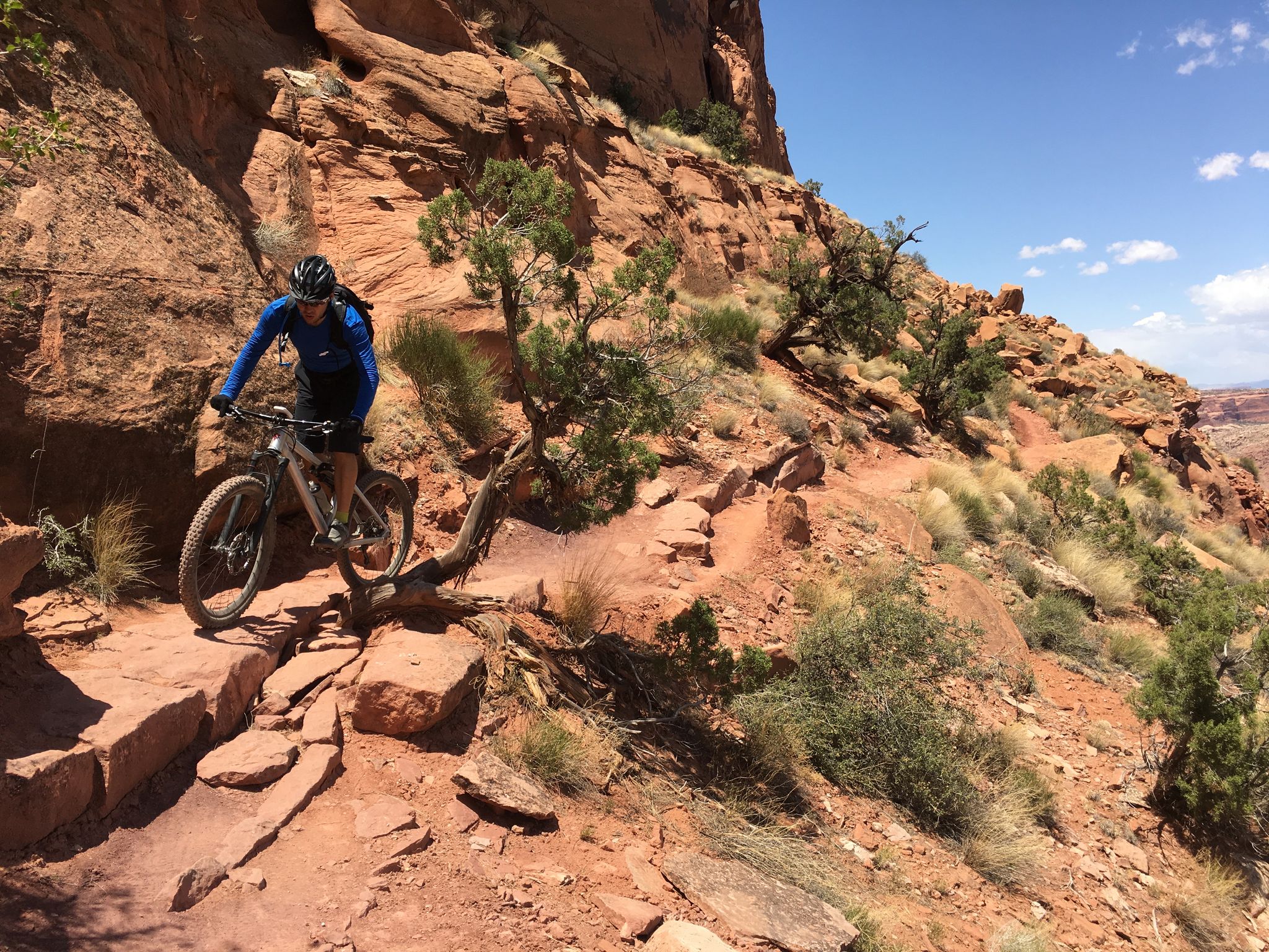 Mountain biker navigates a steep, rocky trail on a sunny day with red cliffs. - Portal Overlook loop from Portal Trail