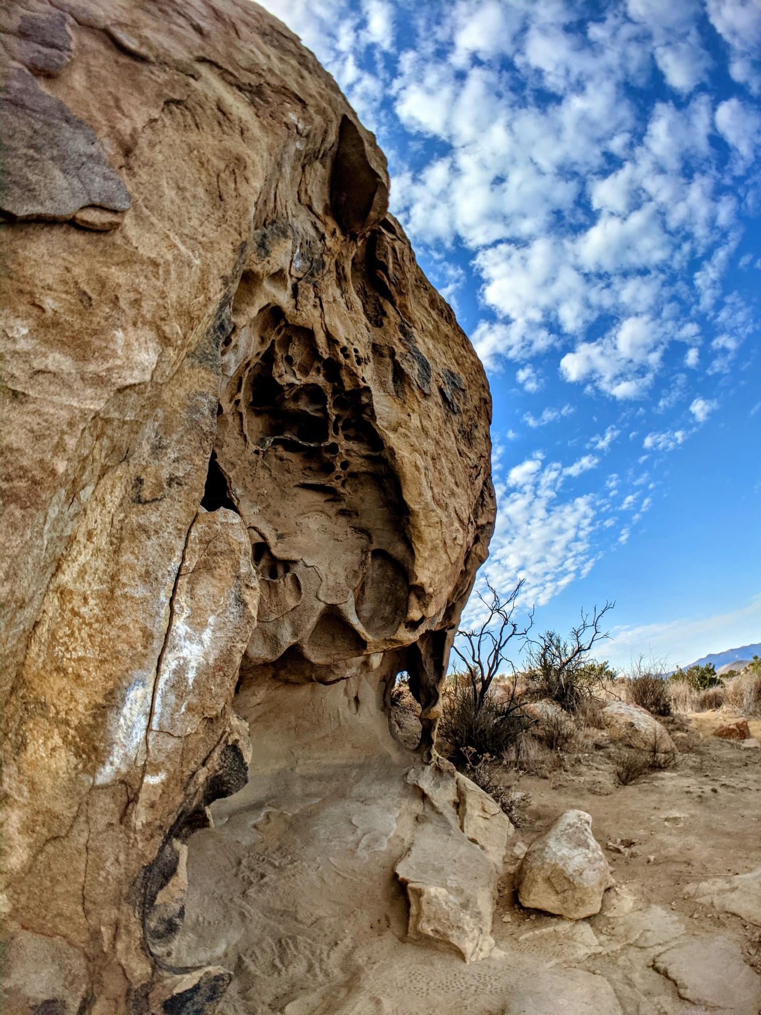 Massive textured rock face with natural caves under a sunny, cloudy sky.