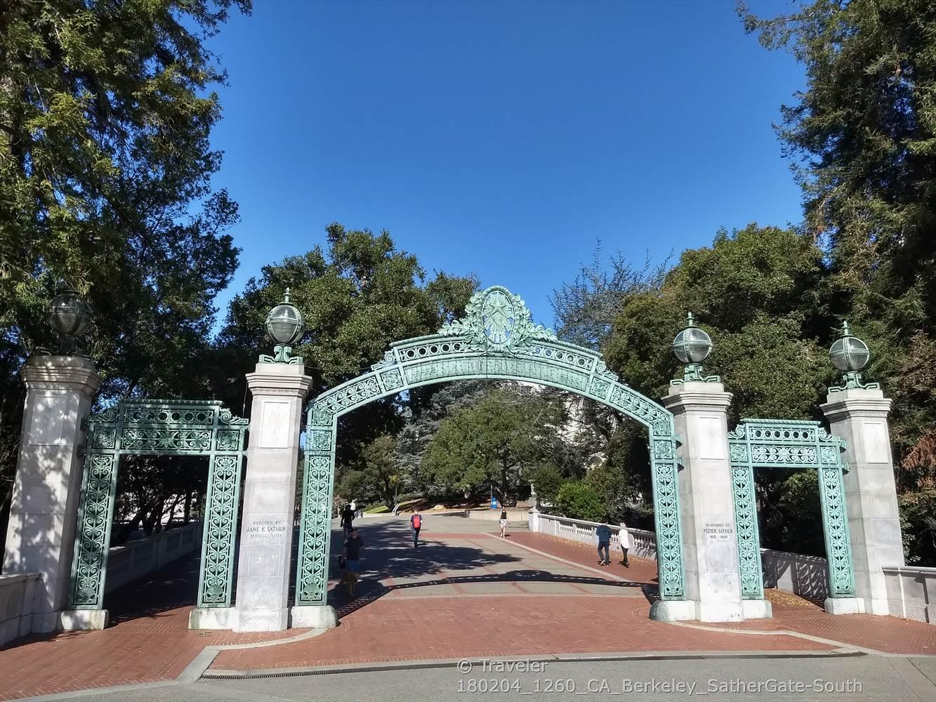 Ornate green archway over a brick path with people walking under a clear sky.