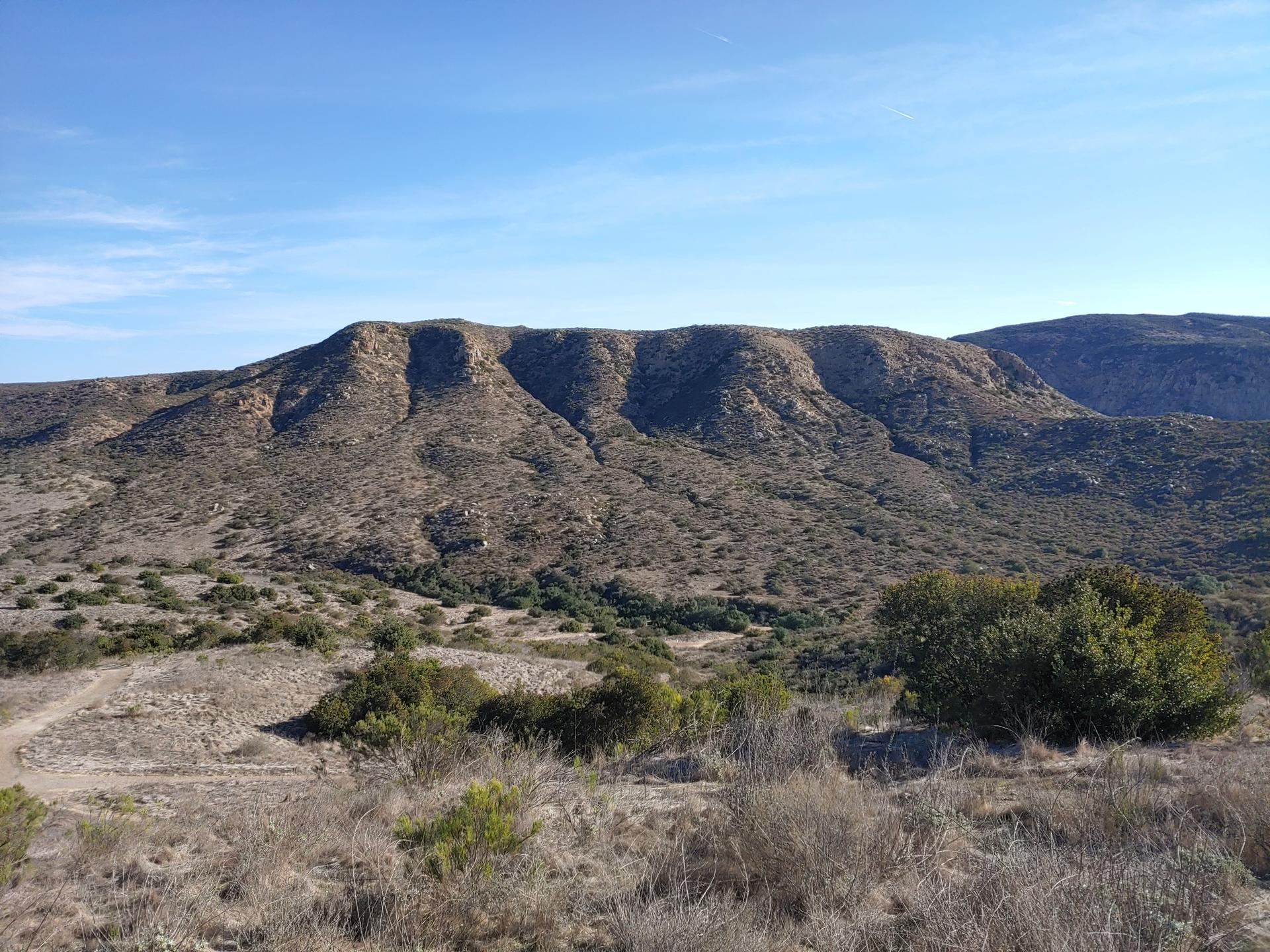 Expansive view of dry, rugged mountains and scrubland under a clear sky.