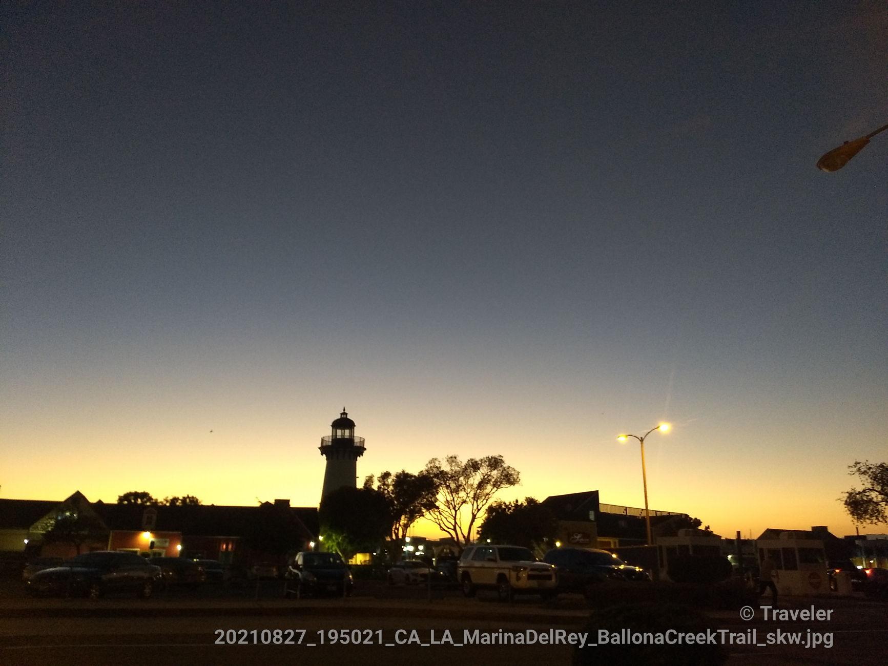 Lighthouse and buildings silhouetted against a vibrant orange and blue sunset sky.