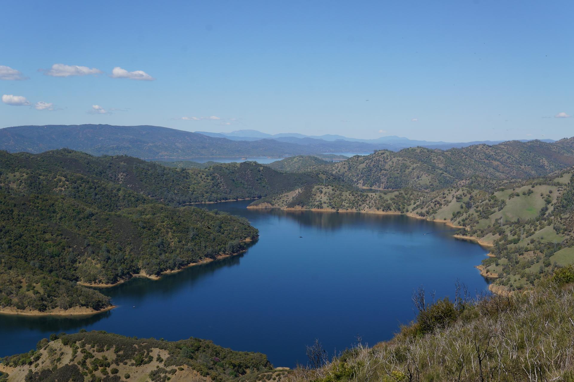 Expansive view of a deep blue lake nestled among green mountains under clear skies.