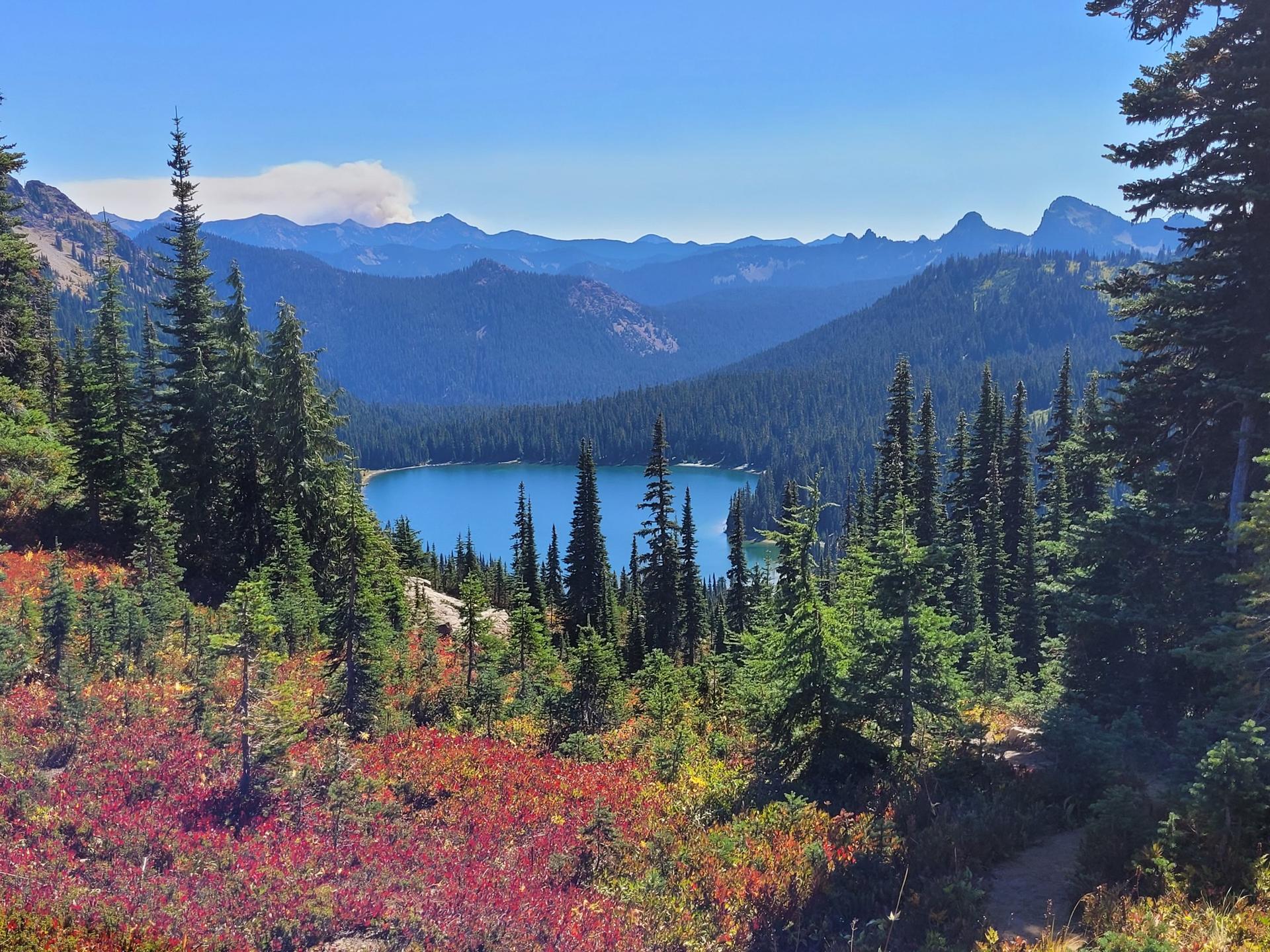 Vibrant red and green foliage frames a deep blue lake and distant mountains.