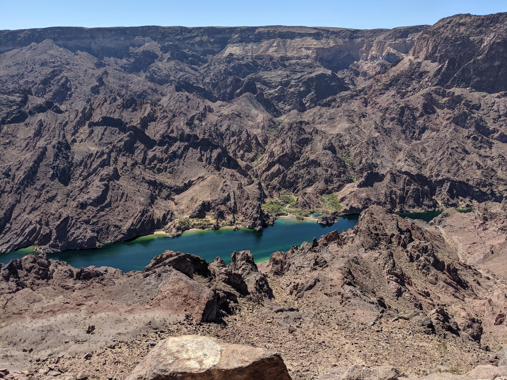 A deep canyon with a winding blue-green river and rugged, dark mountains.