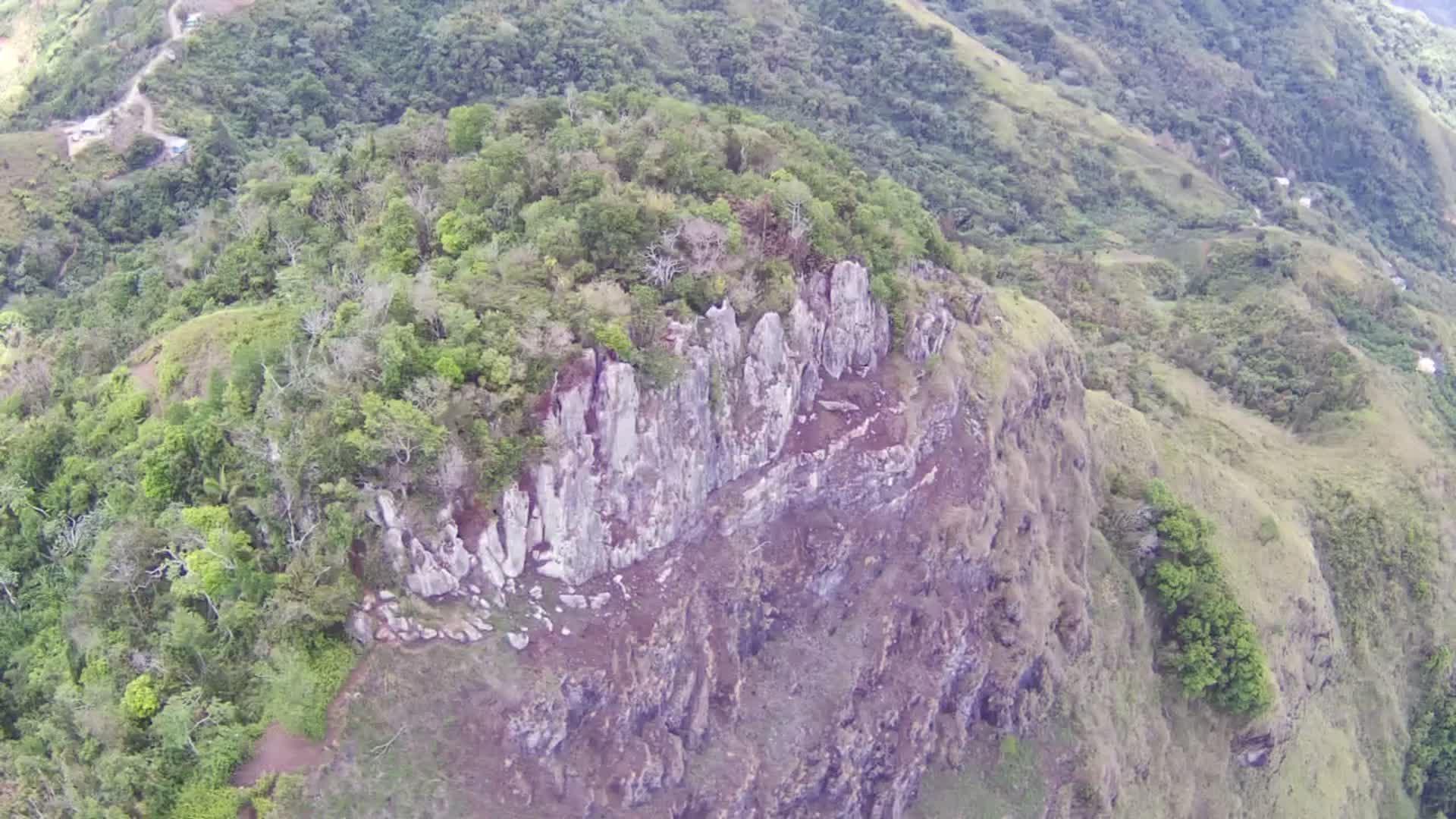 Aerial view of a rugged, rocky cliff face on a steep, green hillside.