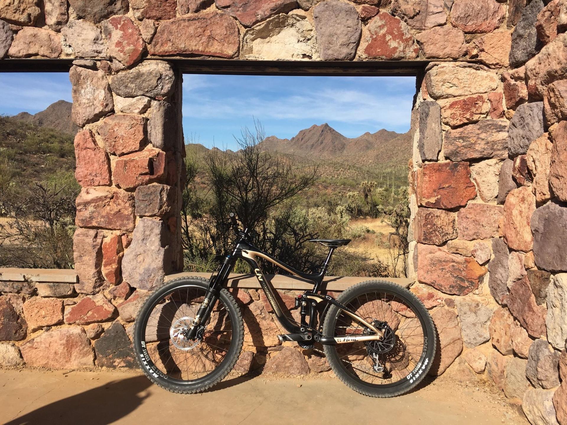 Mountain bike rests against a stone wall, framing a sunny desert mountain view.