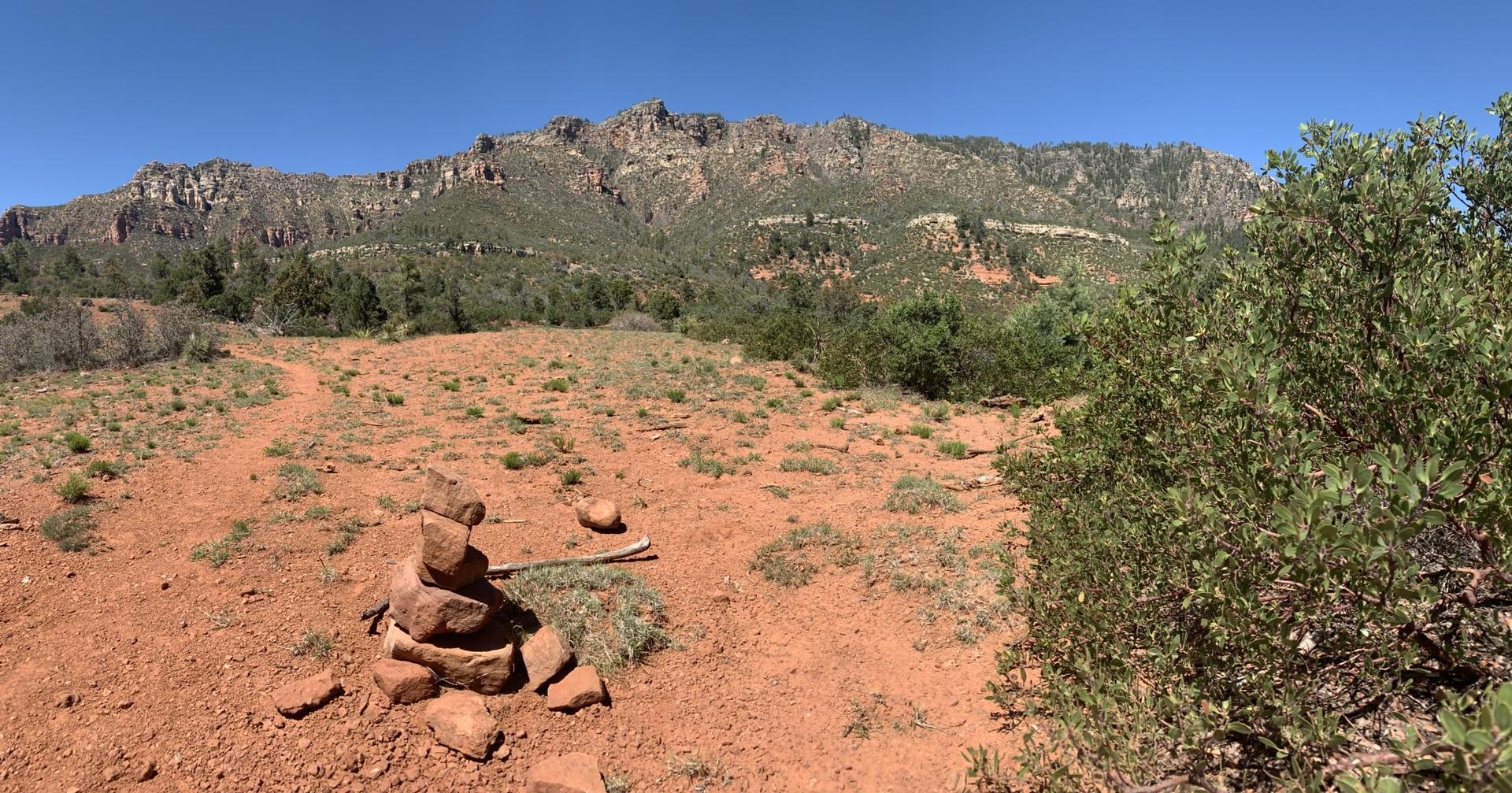 Rock cairn on a red dirt path with a large rocky mountain range.