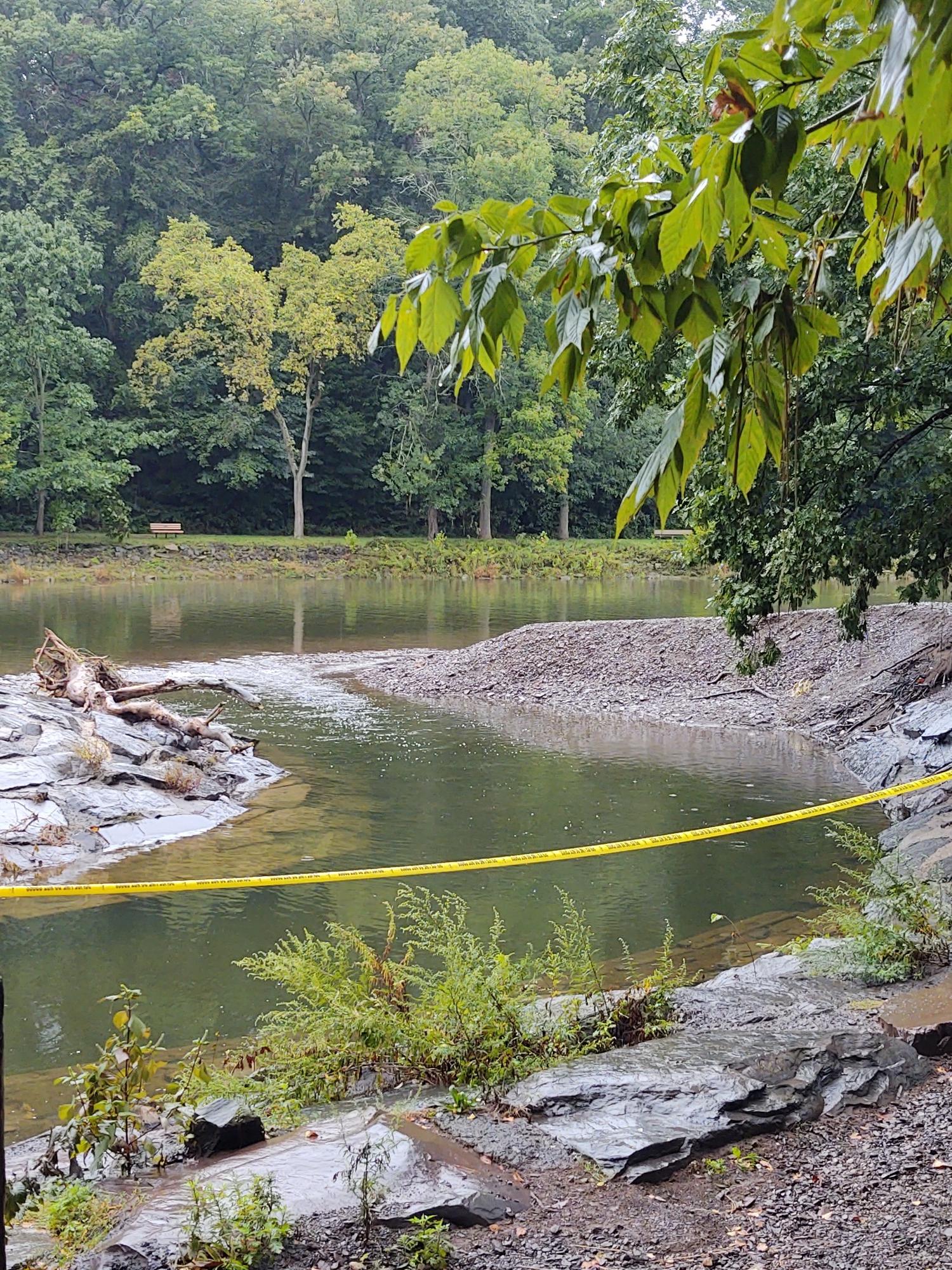 Overcast view of a river with rocky banks and yellow caution tape.
