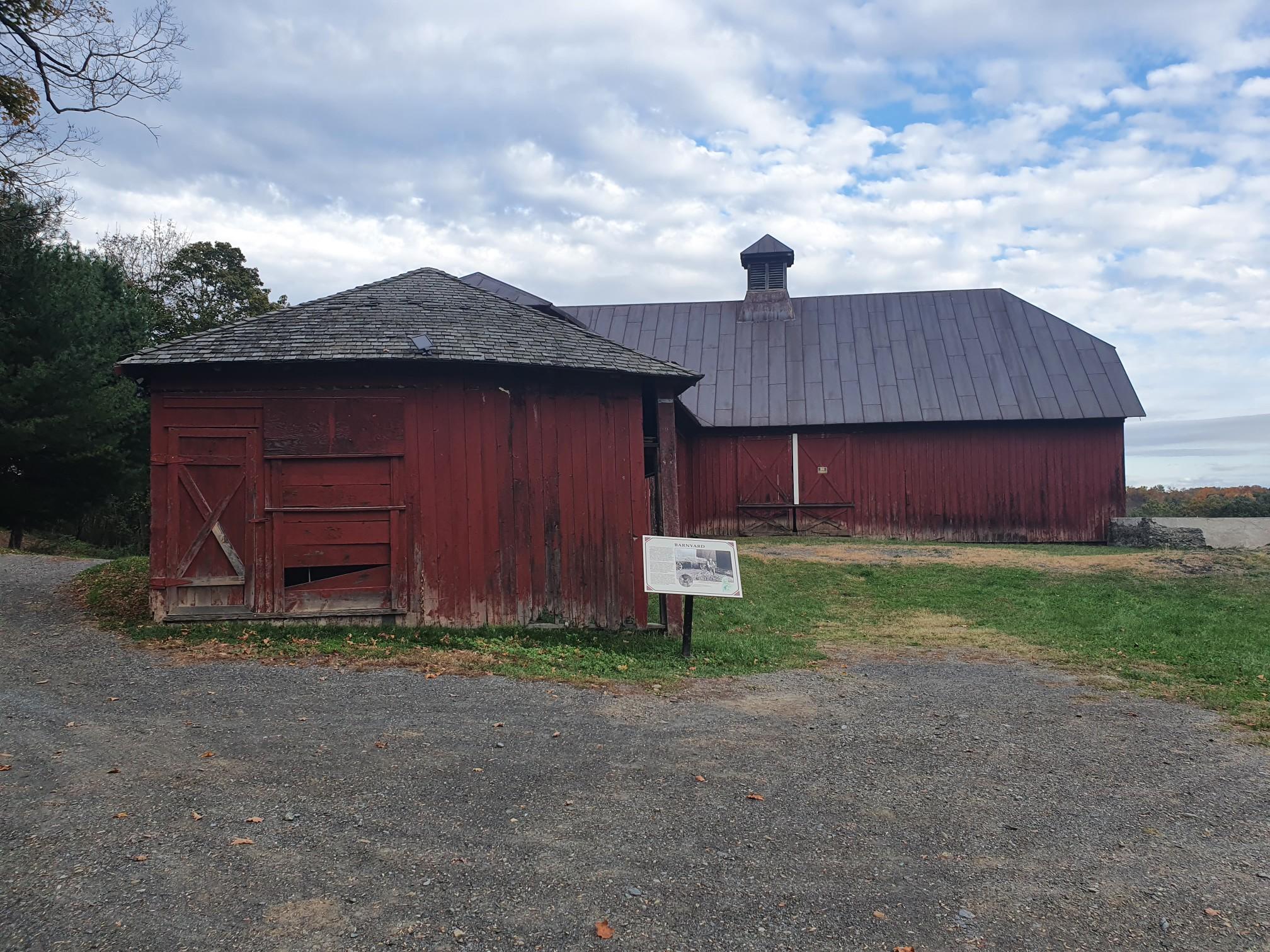 Two old red farm buildings under a cloudy sky.