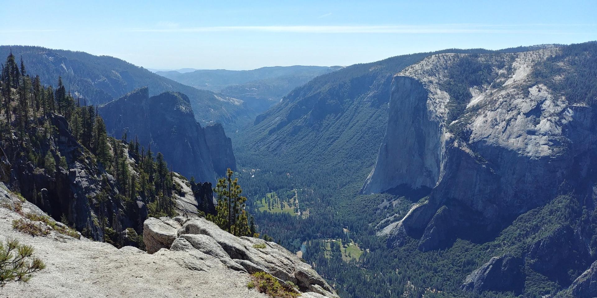 Panoramic view of a deep, forested valley with towering cliffs under clear skies.