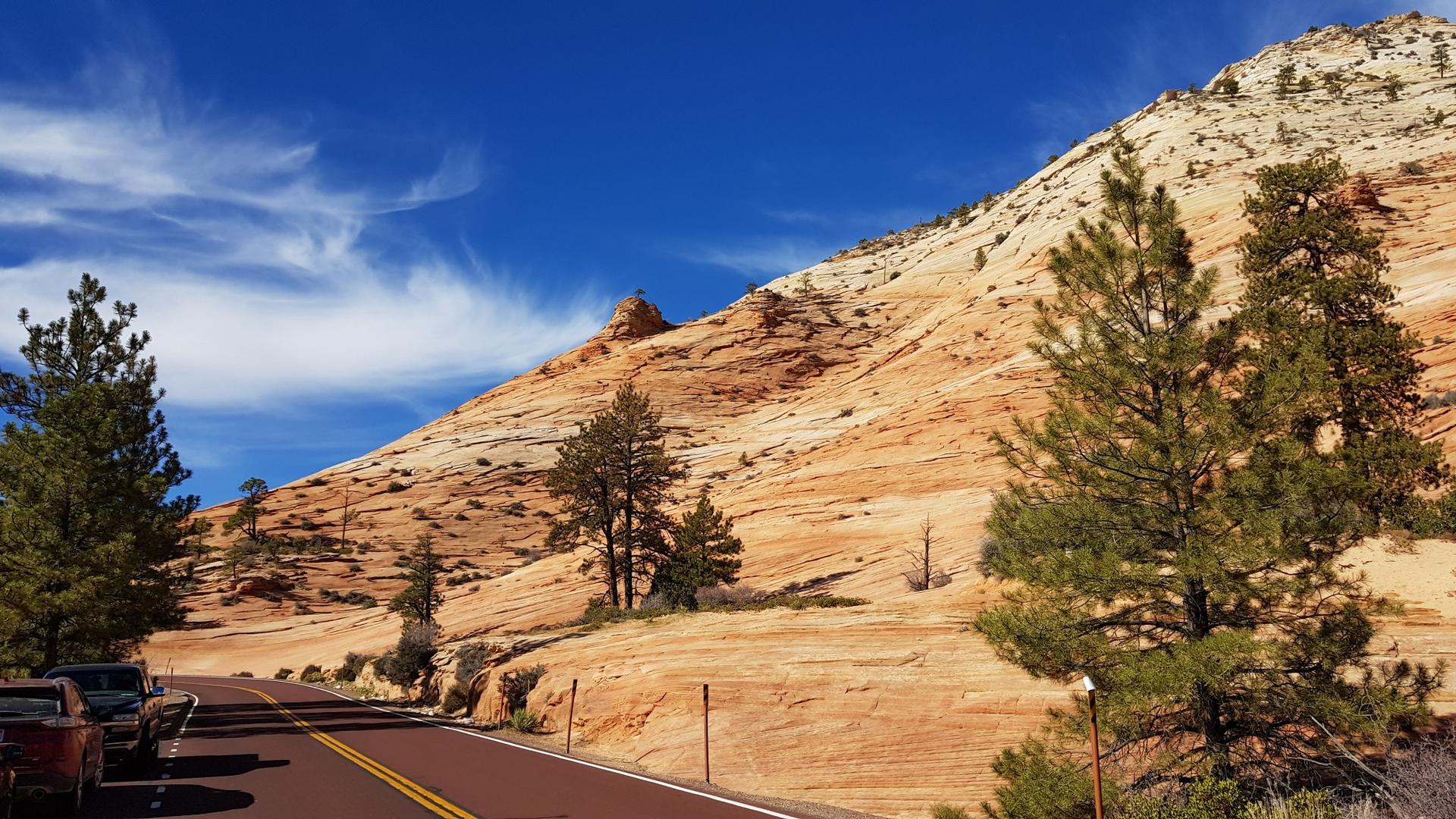 Winding road next to a massive striped rock formation under a blue sky.