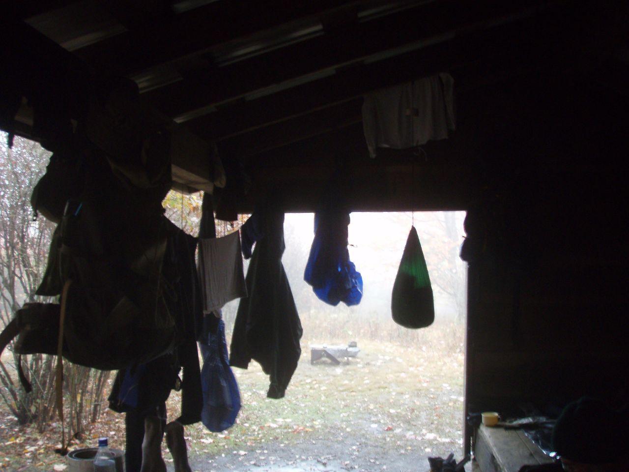 Dark shelter interior with clothes drying, looking out at a foggy day.