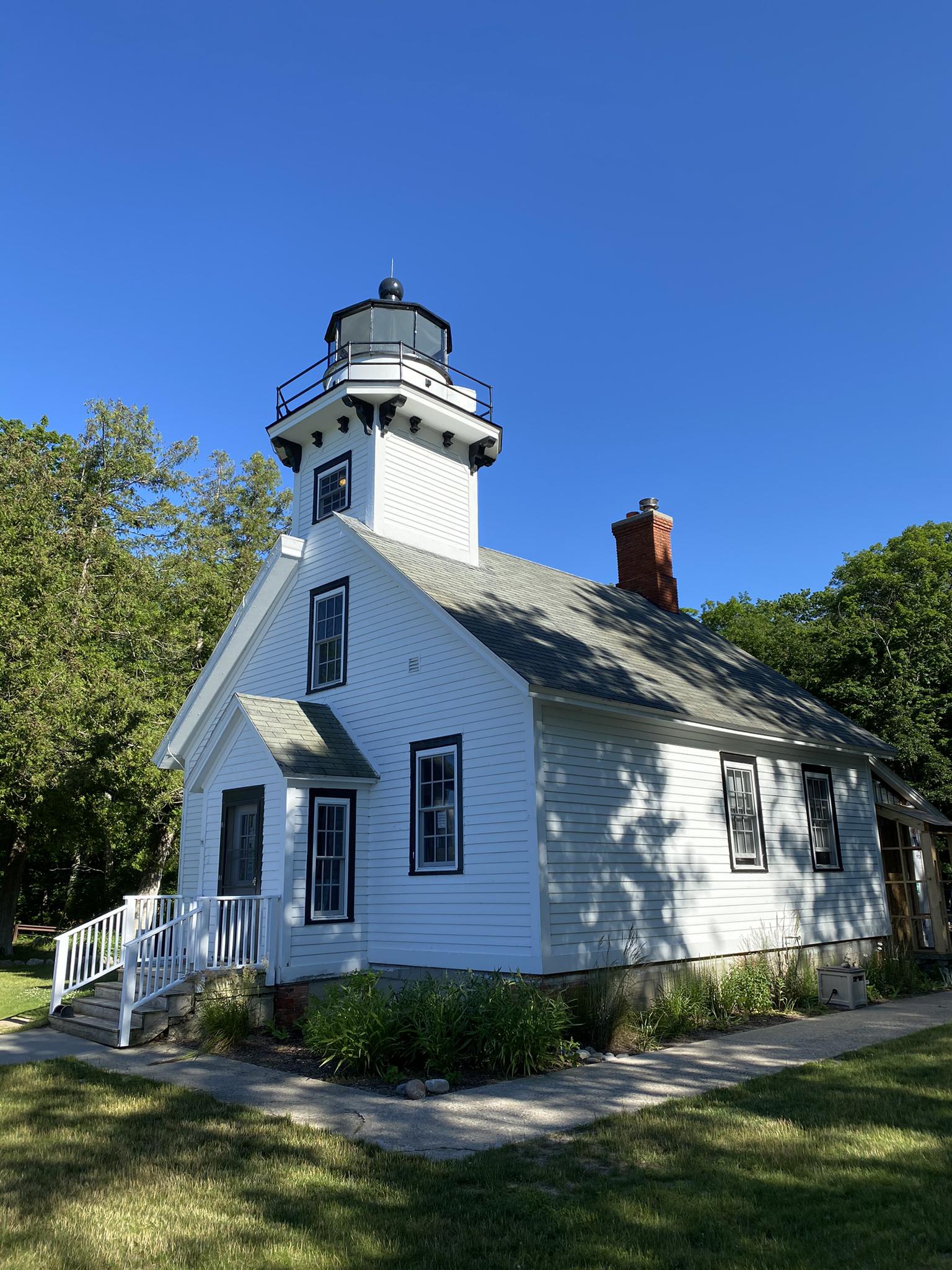 White lighthouse building with a black top under a clear blue sky.